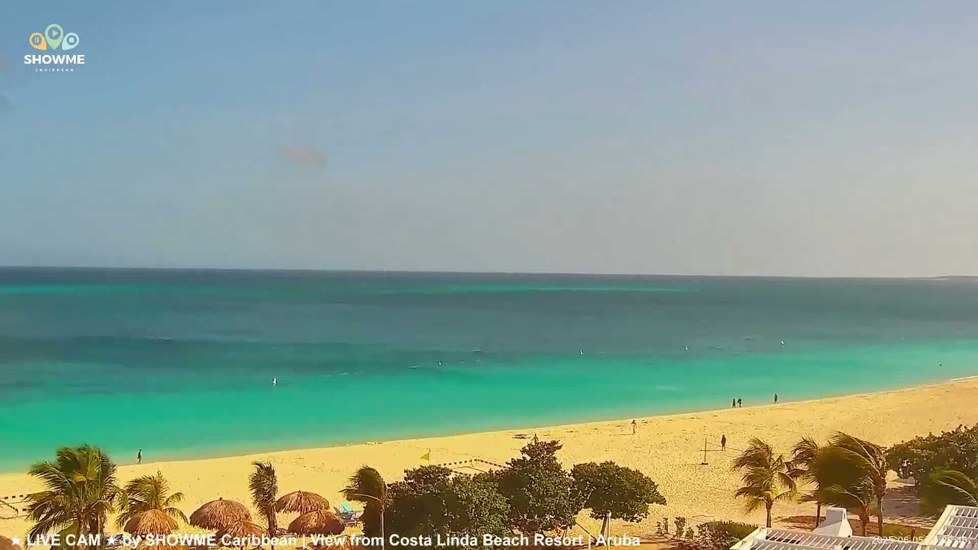 A beach with light-colored sand and turquoise water stretches to the horizon under a clear sky.