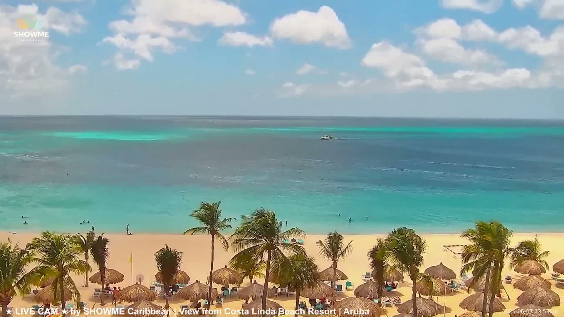A beach with palm trees and thatched umbrellas sits beside a calm, turquoise ocean under a partly cloudy sky.
