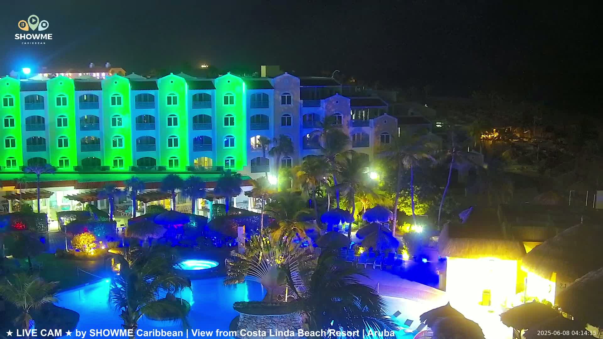 A brightly lit resort at night, featuring a large pool and a multi-story building illuminated in green and blue hues.