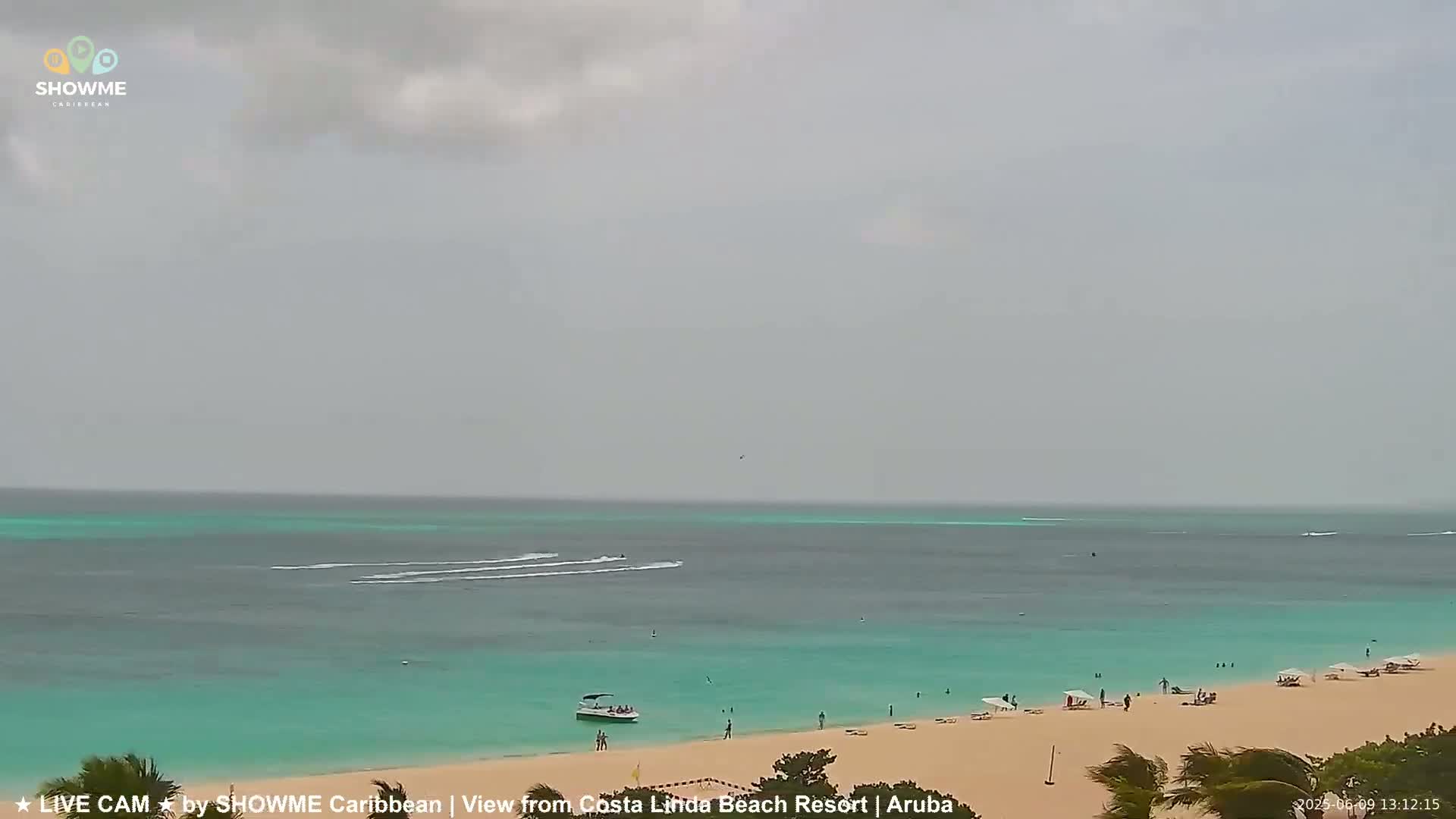 A beach with turquoise water and a few people on the sand under an overcast sky.