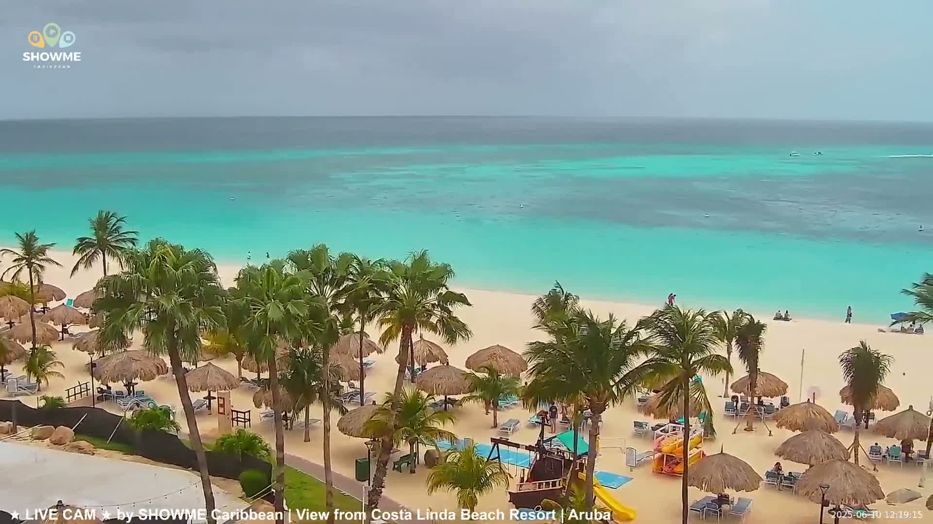 A beach with turquoise water, palm trees, and thatched umbrellas under an overcast sky.
