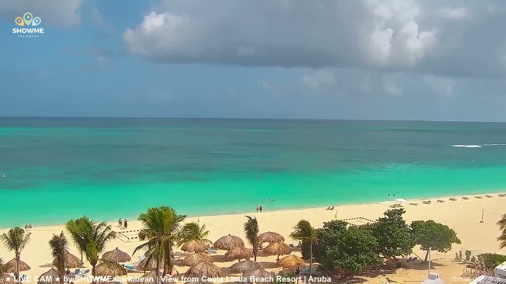 A partly cloudy day shows a beach with turquoise water, palm trees, and beach umbrellas.