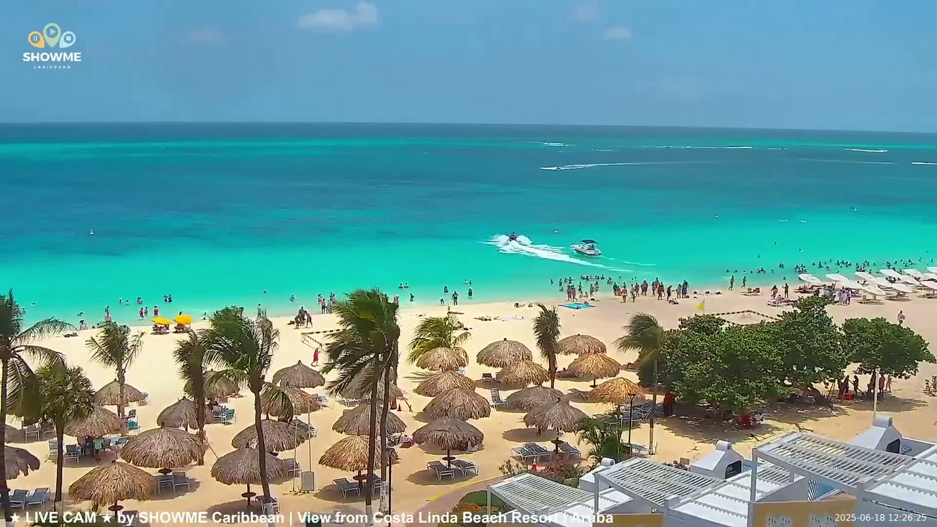 A sunny beach scene shows a white sandy beach with turquoise water, numerous thatched umbrellas, and many people swimming and relaxing.