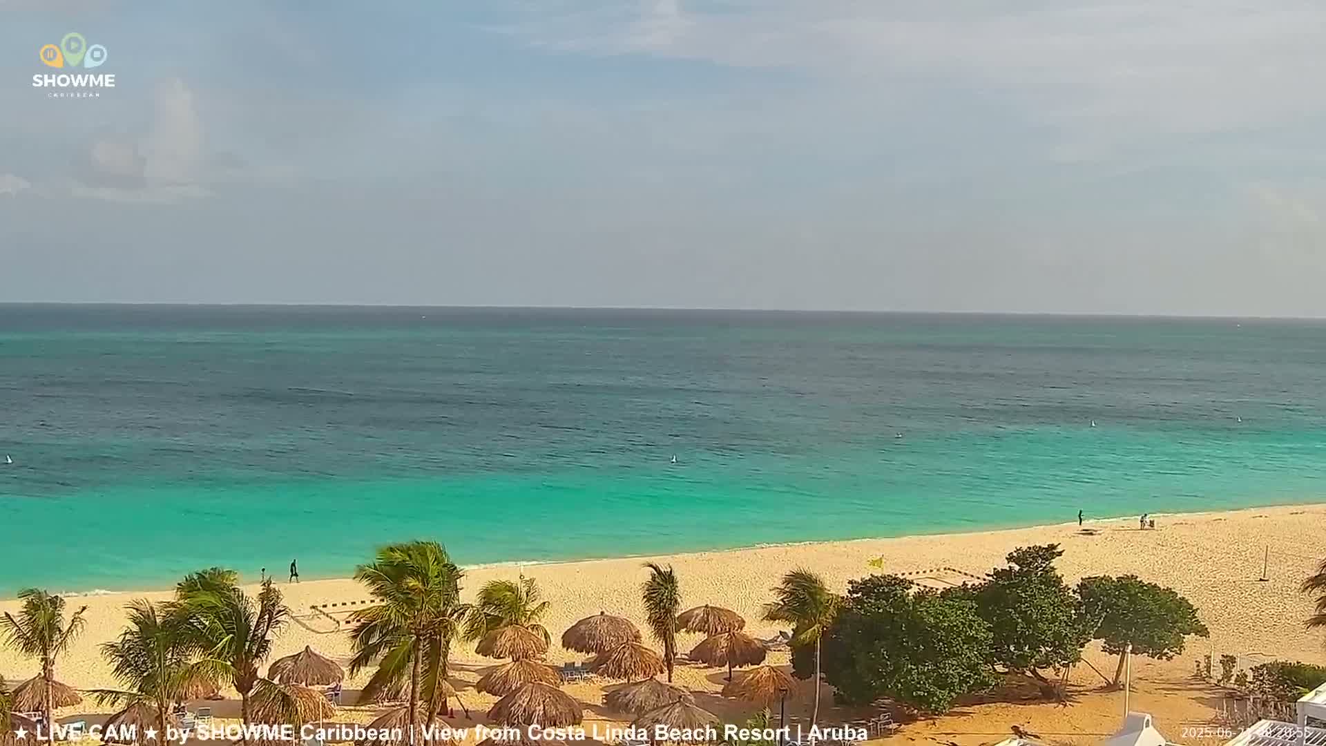 A pristine beach with turquoise water and palm trees under a mostly clear sky.