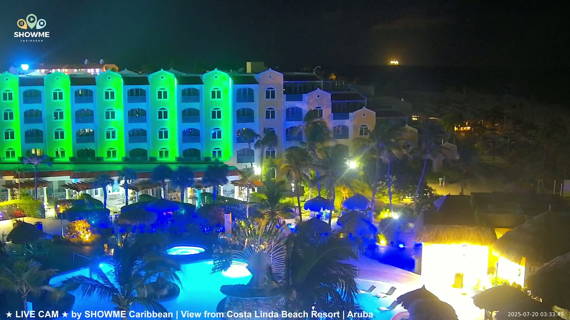 A brightly lit resort at night, featuring a multi-story building with pools and palm trees.