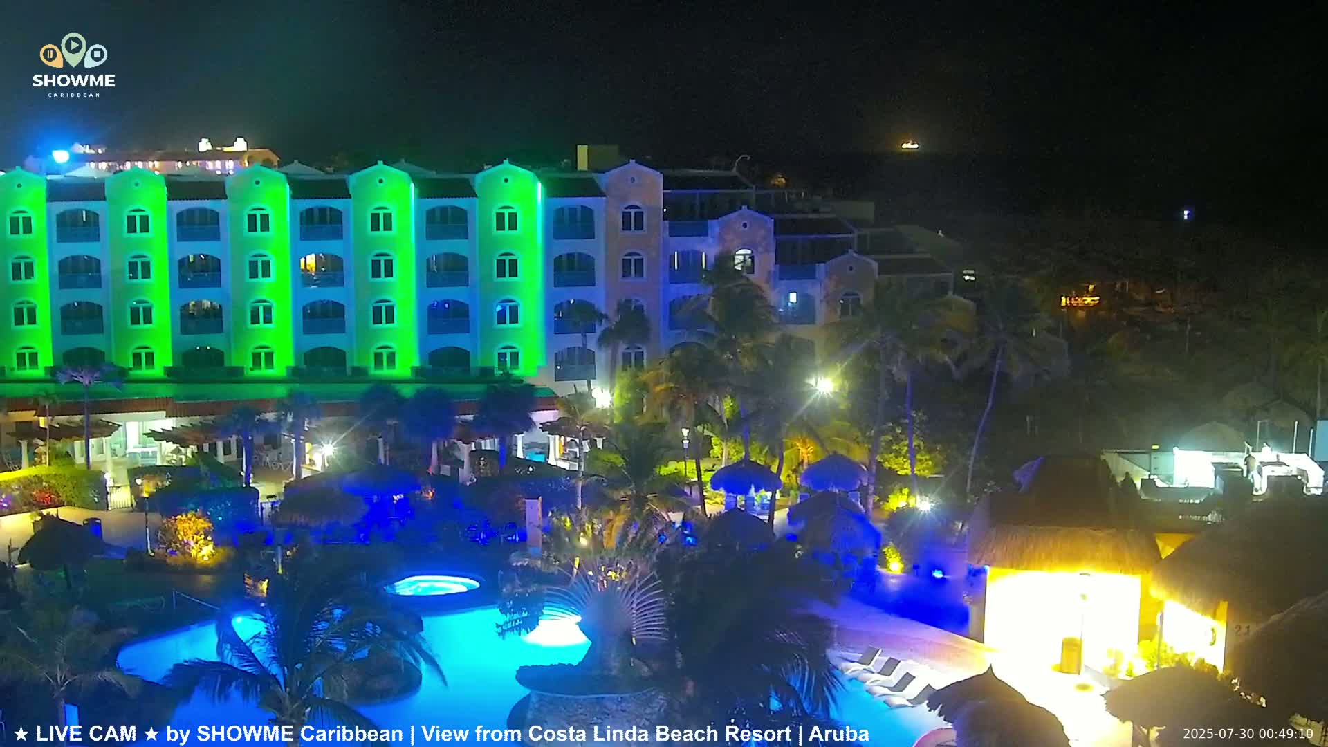 A brightly lit resort at night, featuring a multi-story building with pools and palm trees.