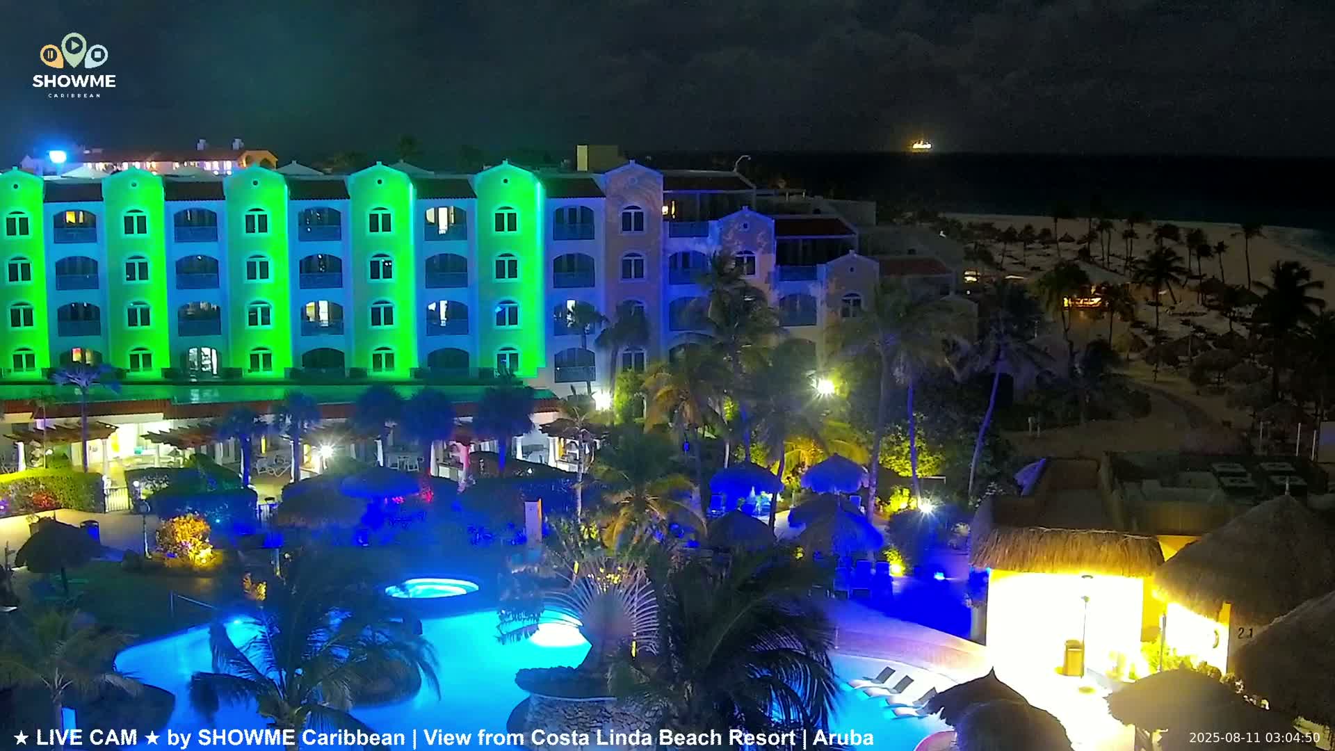 A brightly lit resort at night, with a pool area and a beach visible in the background under a clear, dark sky.