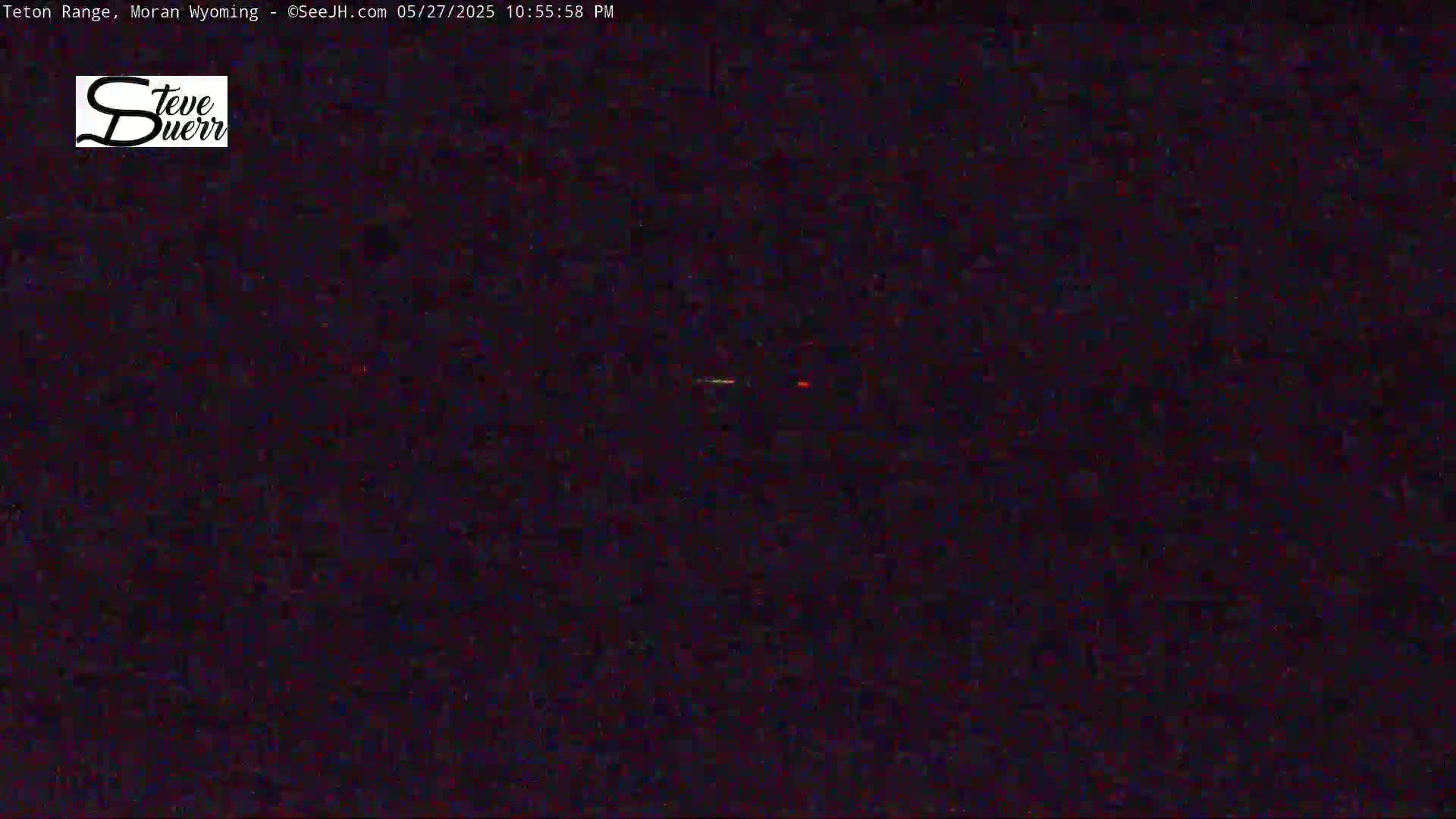 A nighttime image shows a dark, mostly featureless scene with a few faint lights visible in the distance.