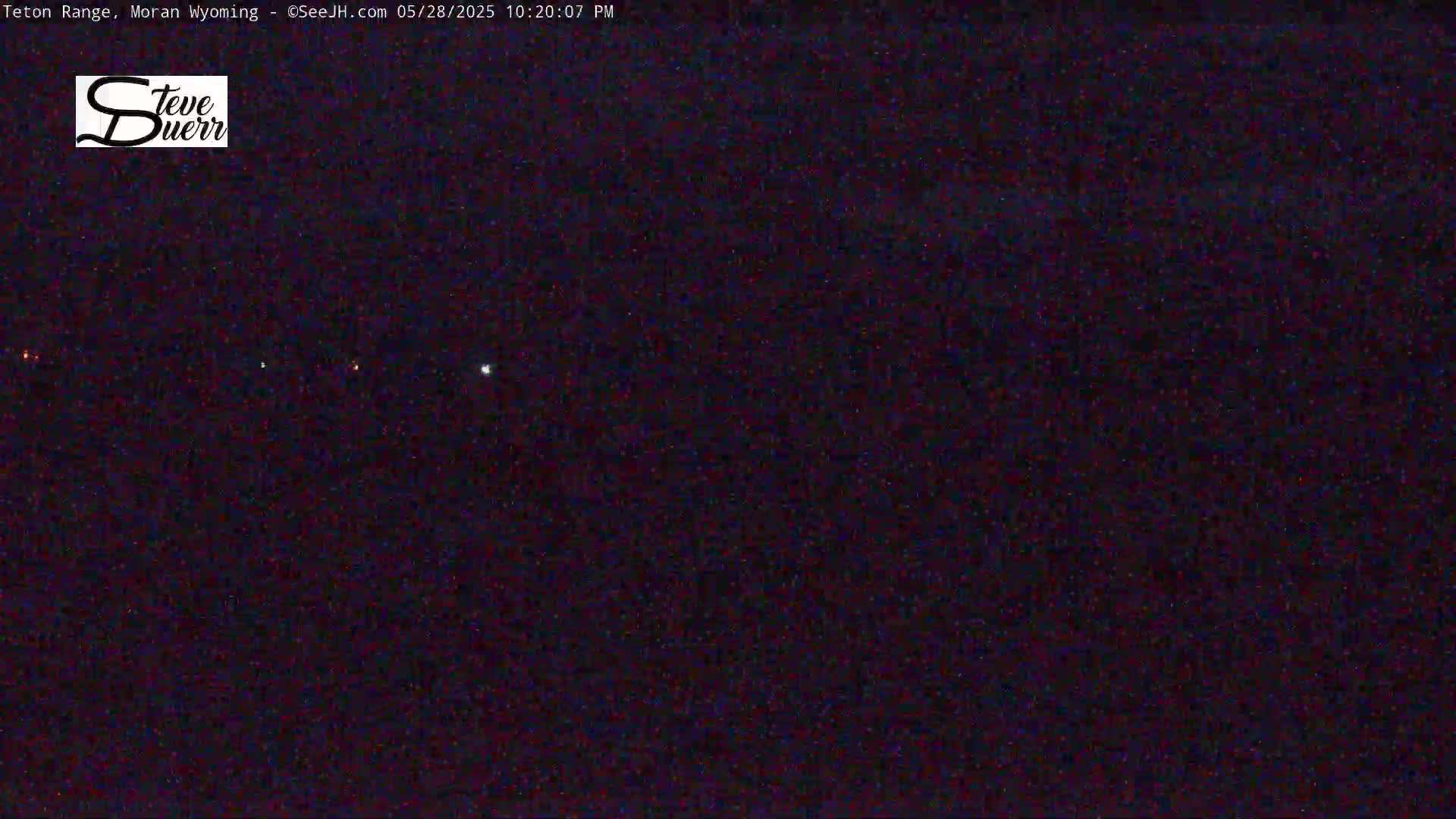 A nighttime, dark scene shows a few distant lights and stars in a dark sky.