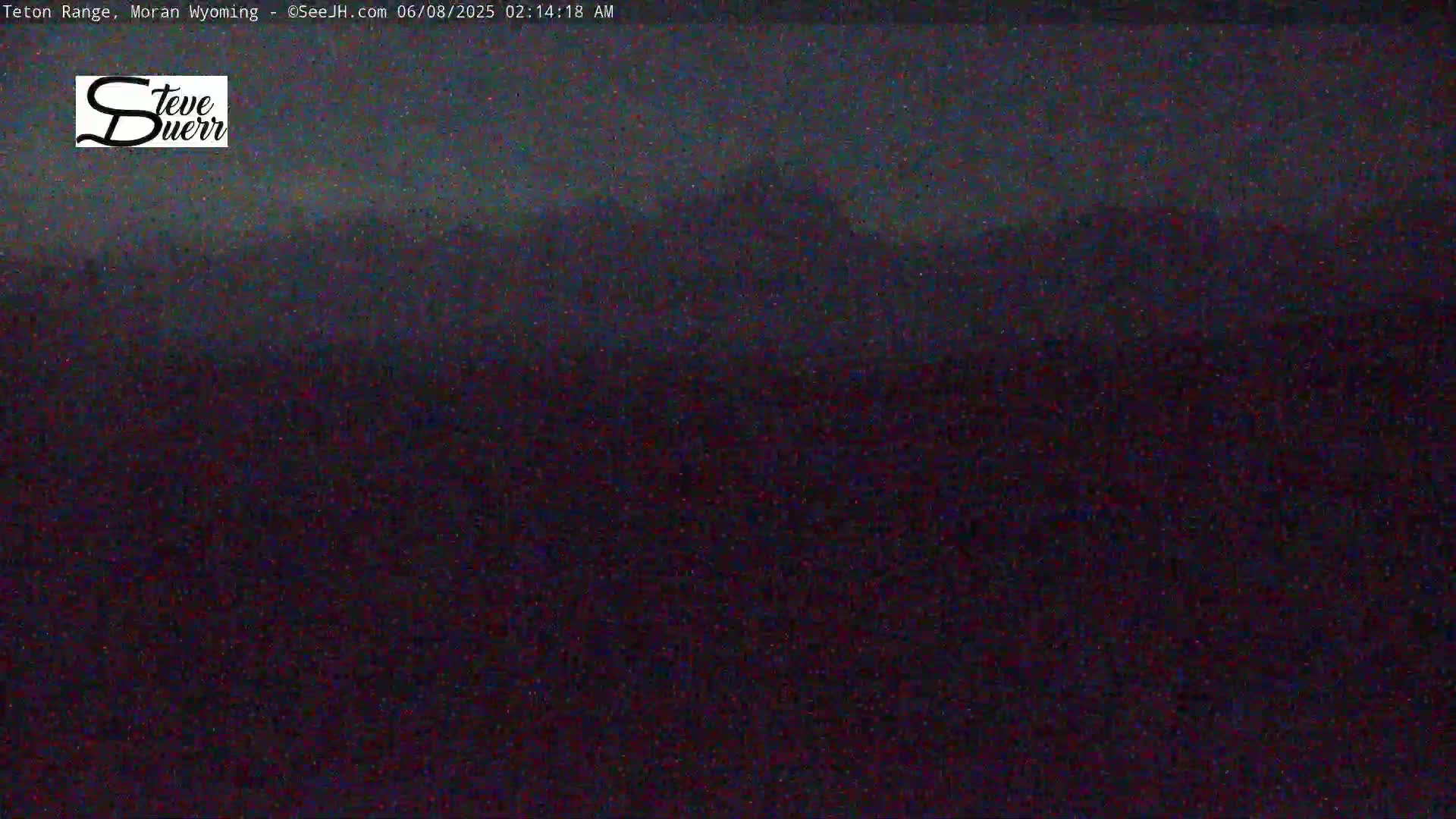 A dark, nighttime view of a mountain range under a mostly clear sky.