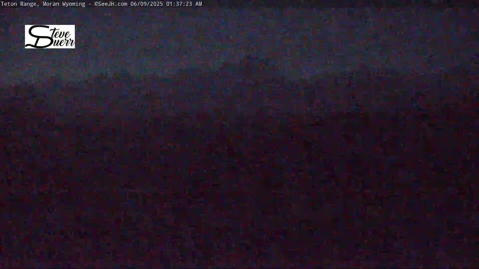 A dark, blurry image of a landscape at night, possibly showing a mountain range under a dark sky.