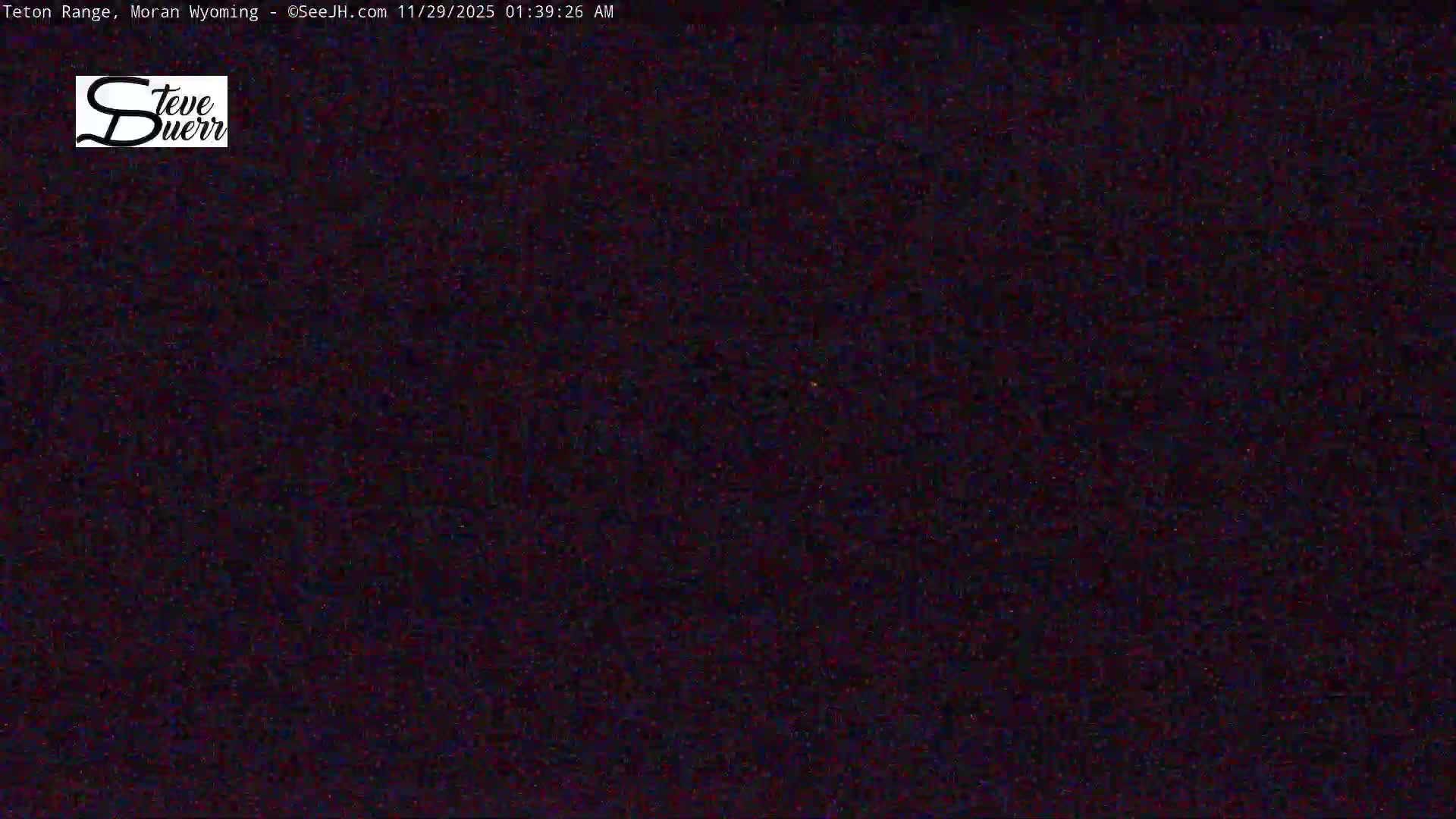 An extremely dark, noisy outdoor scene is visible, illuminated only by a single, tiny, faint yellowish light source, indicating clear night conditions.