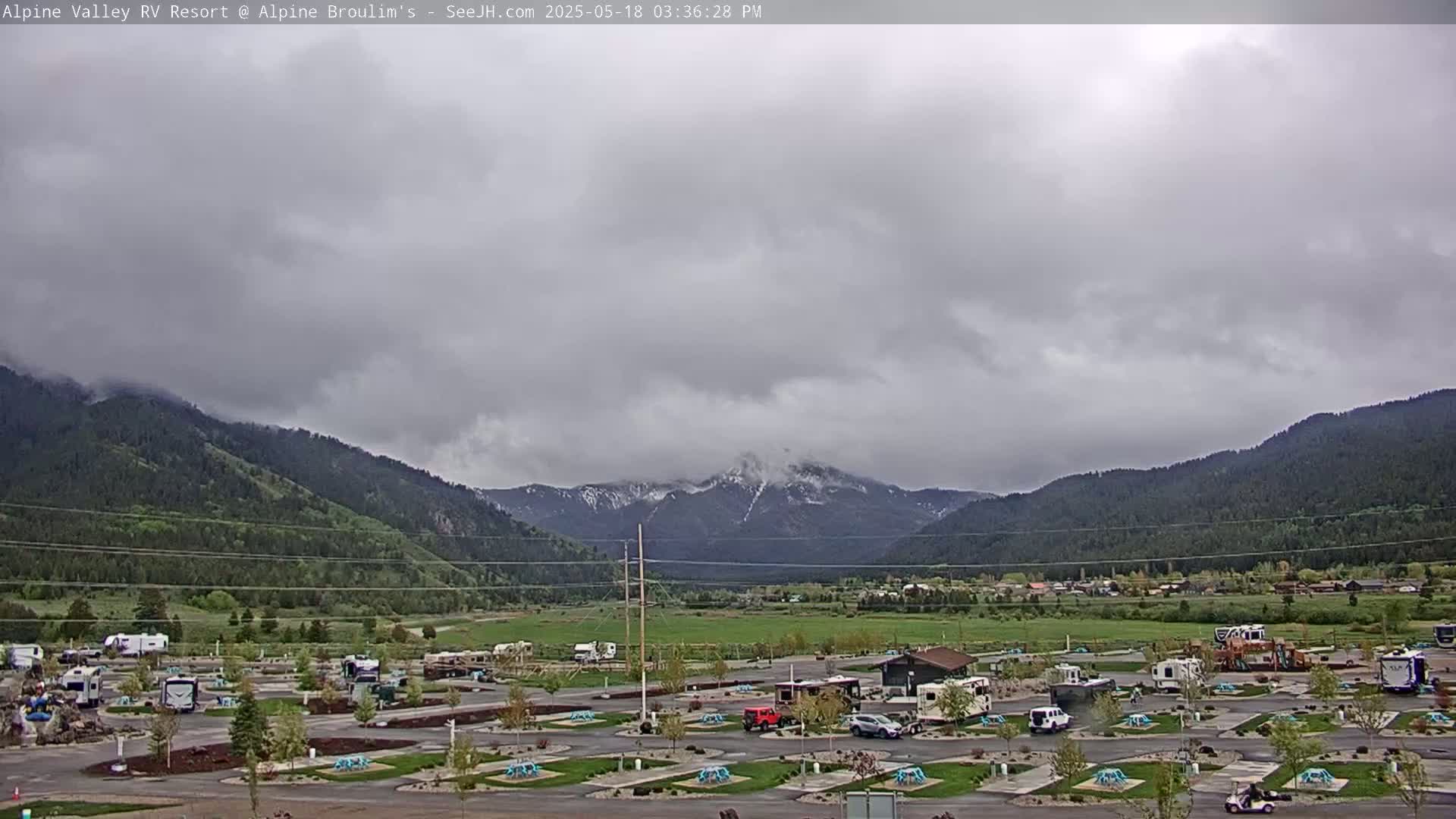 An RV park sits in a valley between snow-capped mountains under an overcast sky.