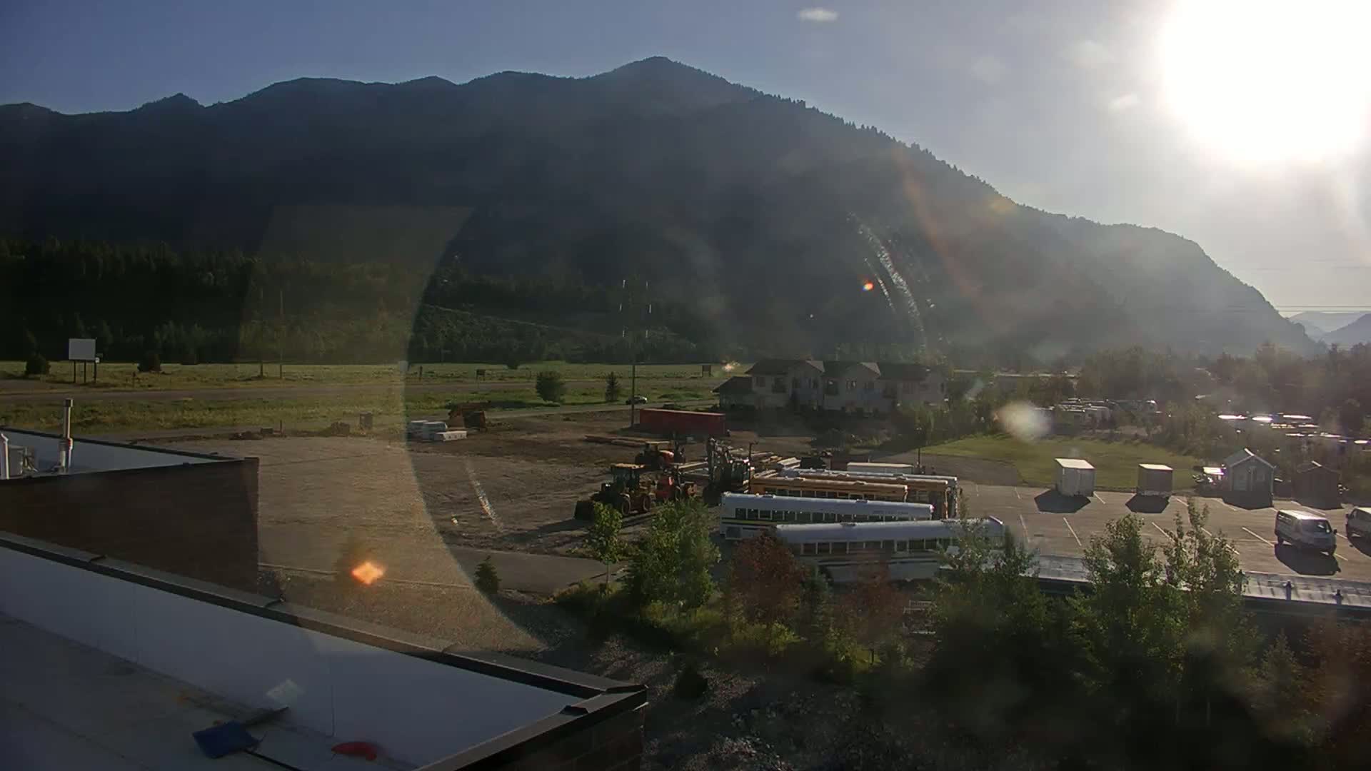 A sunny day reveals a construction site with several pieces of heavy machinery and a line of school buses parked near a mountain range.