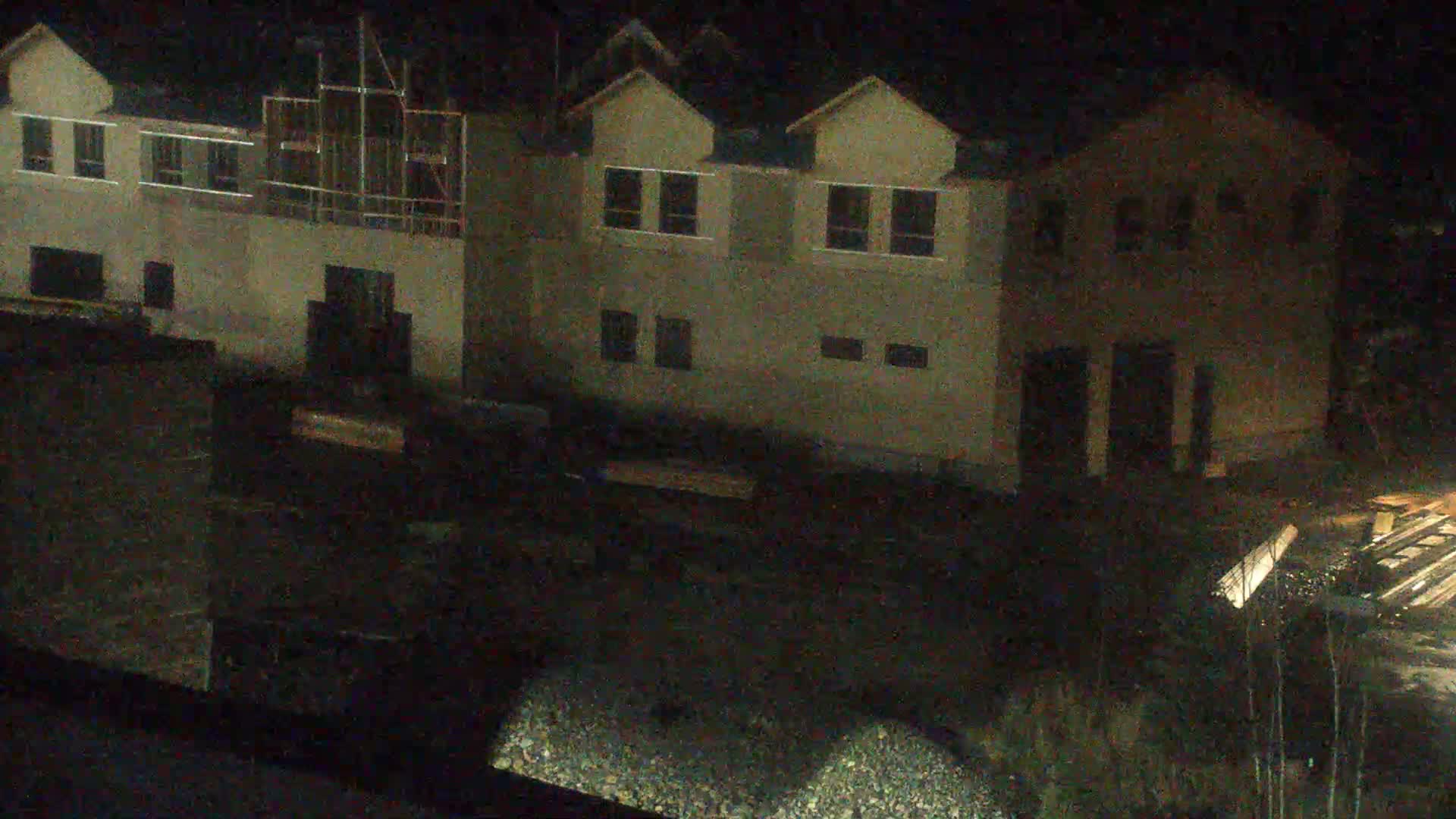A nighttime, low-light view shows a flatbed trailer parked near a construction site with numerous posts and what appears to be a gravel area.