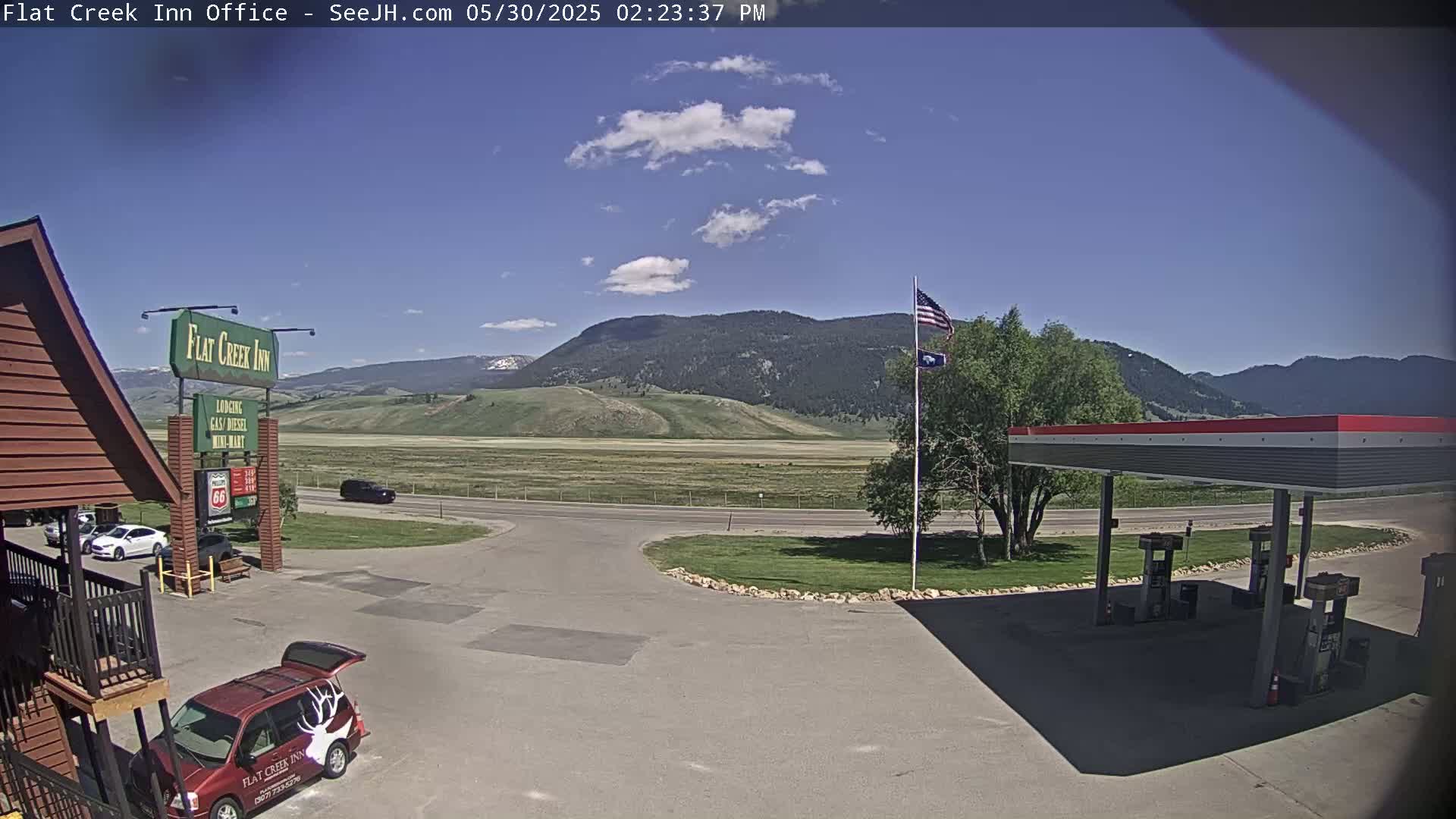A partly cloudy day shows a view of a gas station, a motel, and a mountain range in the distance.