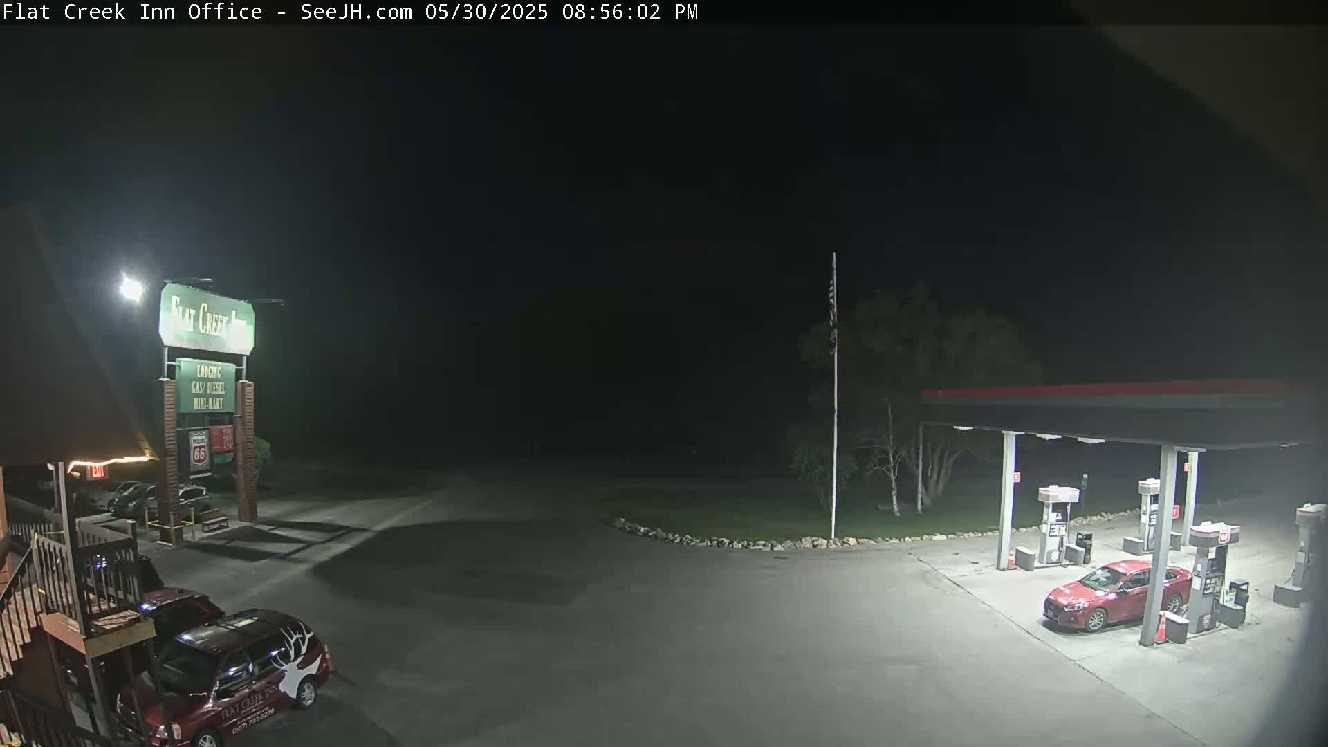 A nighttime view of a gas station and motel parking lot with a red car parked at a gas pump.