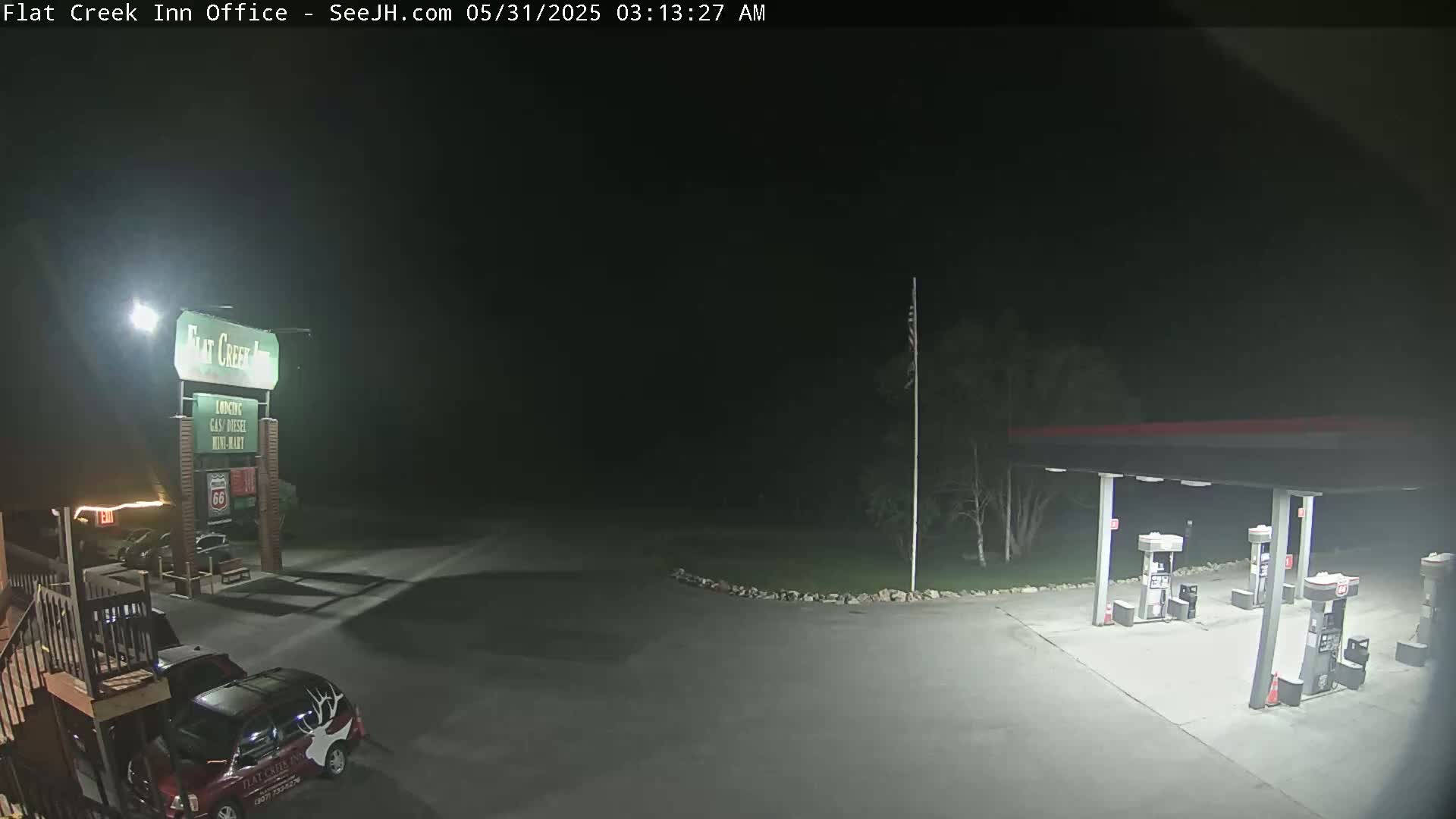 A nighttime view of a gas station and motel parking lot, illuminated by artificial lights.