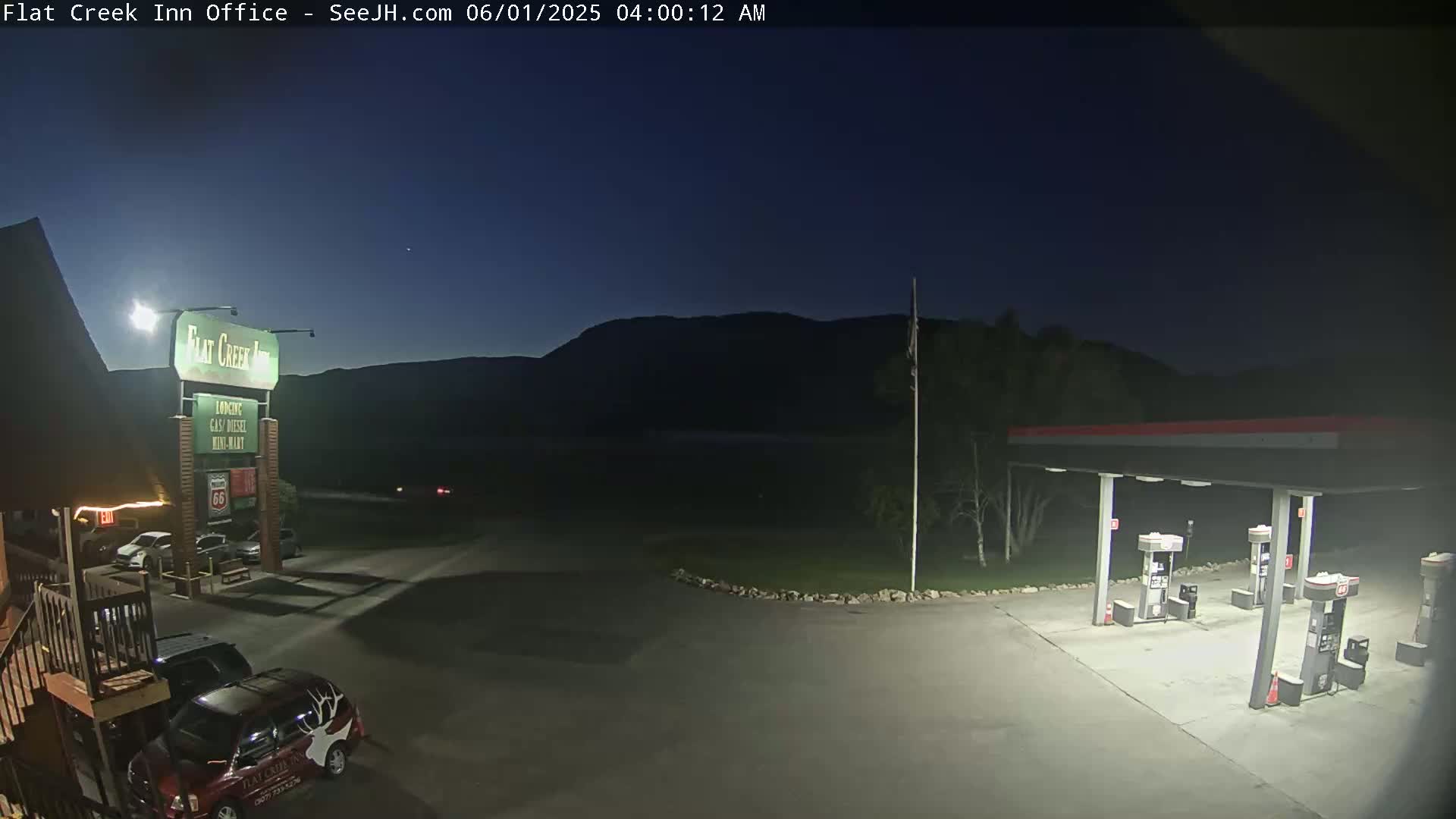 A gas station and motel are visible under a dark, night sky with a mountain range in the background.