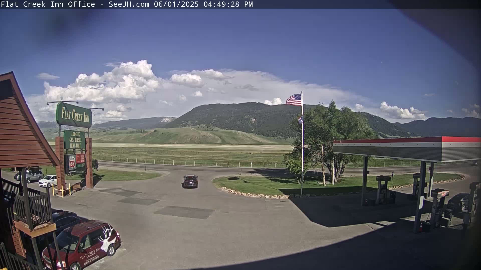A partly cloudy day shows a view of a gas station and inn, with a flat valley and mountains in the background.