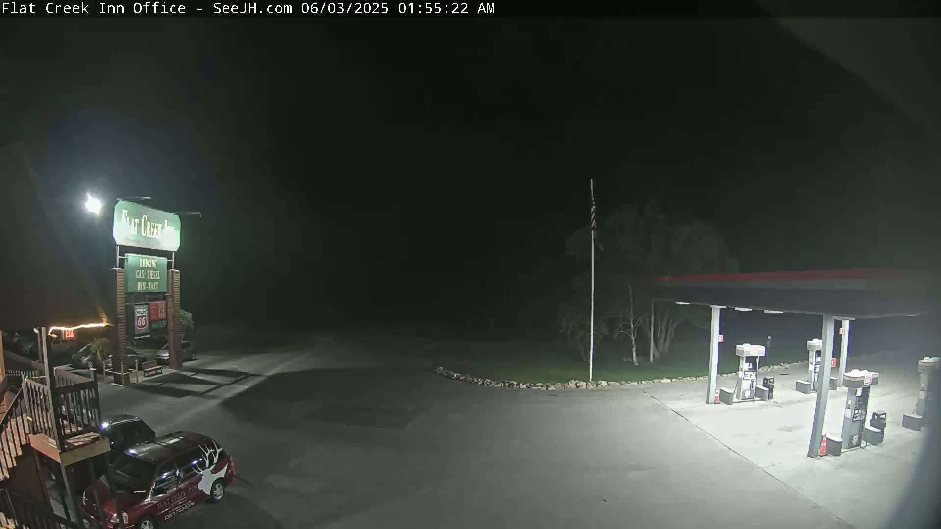 A nighttime view of a gas station and motel parking lot with a few vehicles present under dark skies.
