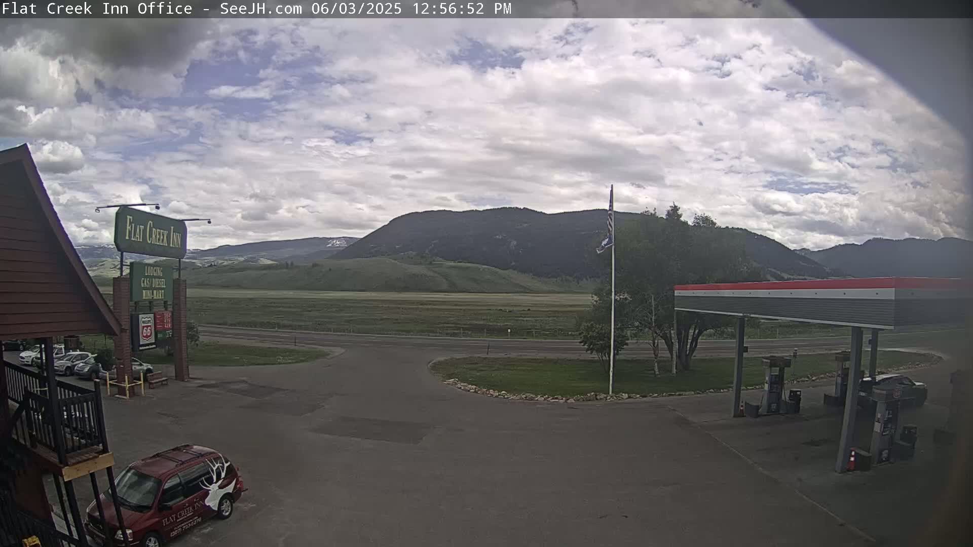 A partly cloudy day shows a gas station and inn parking lot next to a highway, with mountains in the background.