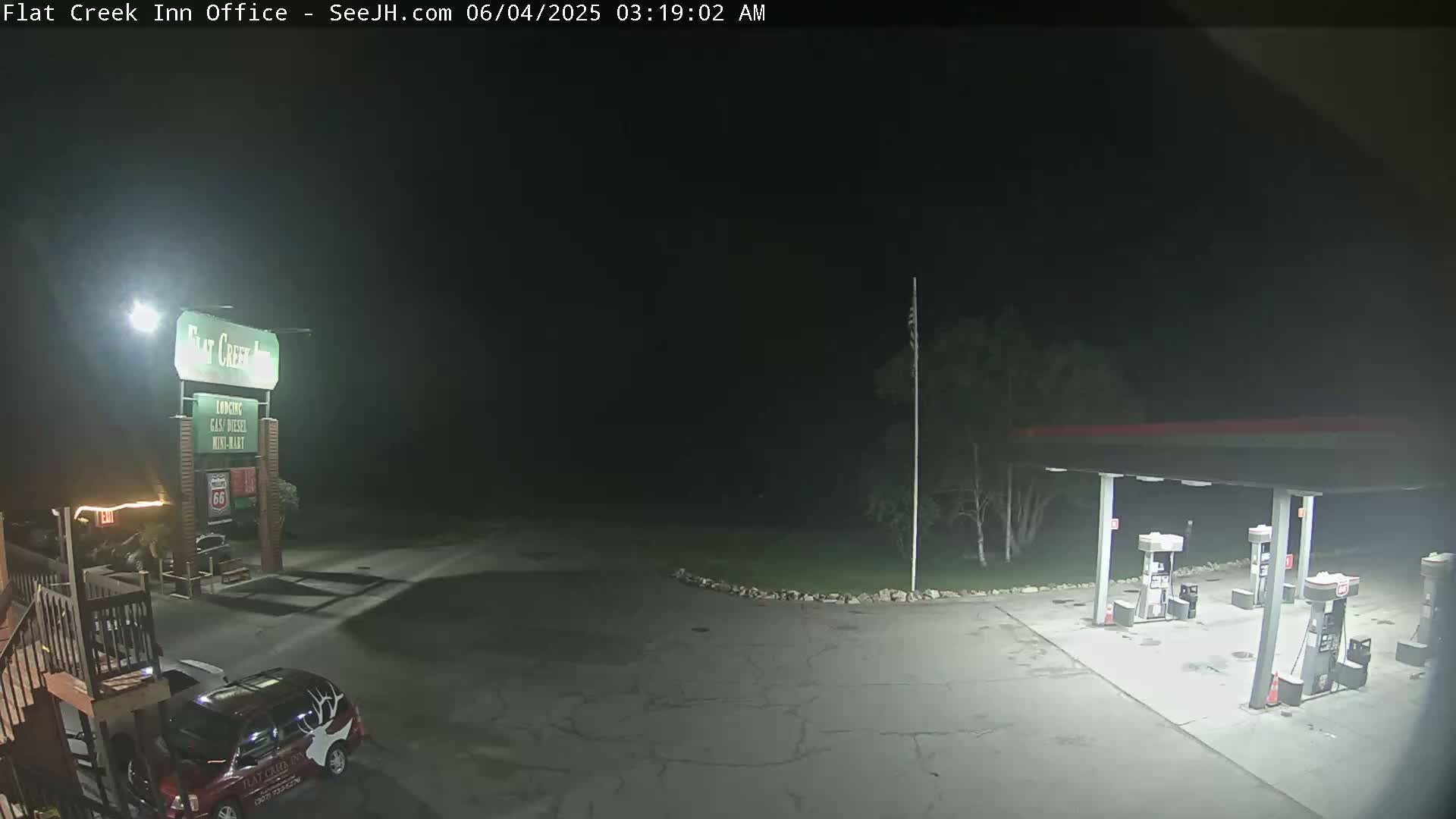 A nighttime view of a gas station and motel parking lot, illuminated by artificial lights.