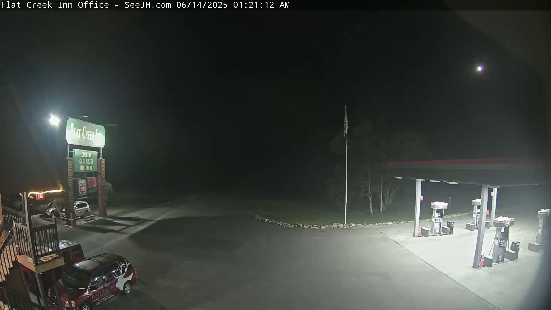A nighttime view of a gas station and motel parking lot, illuminated by artificial light, under a clear, moonlit sky.