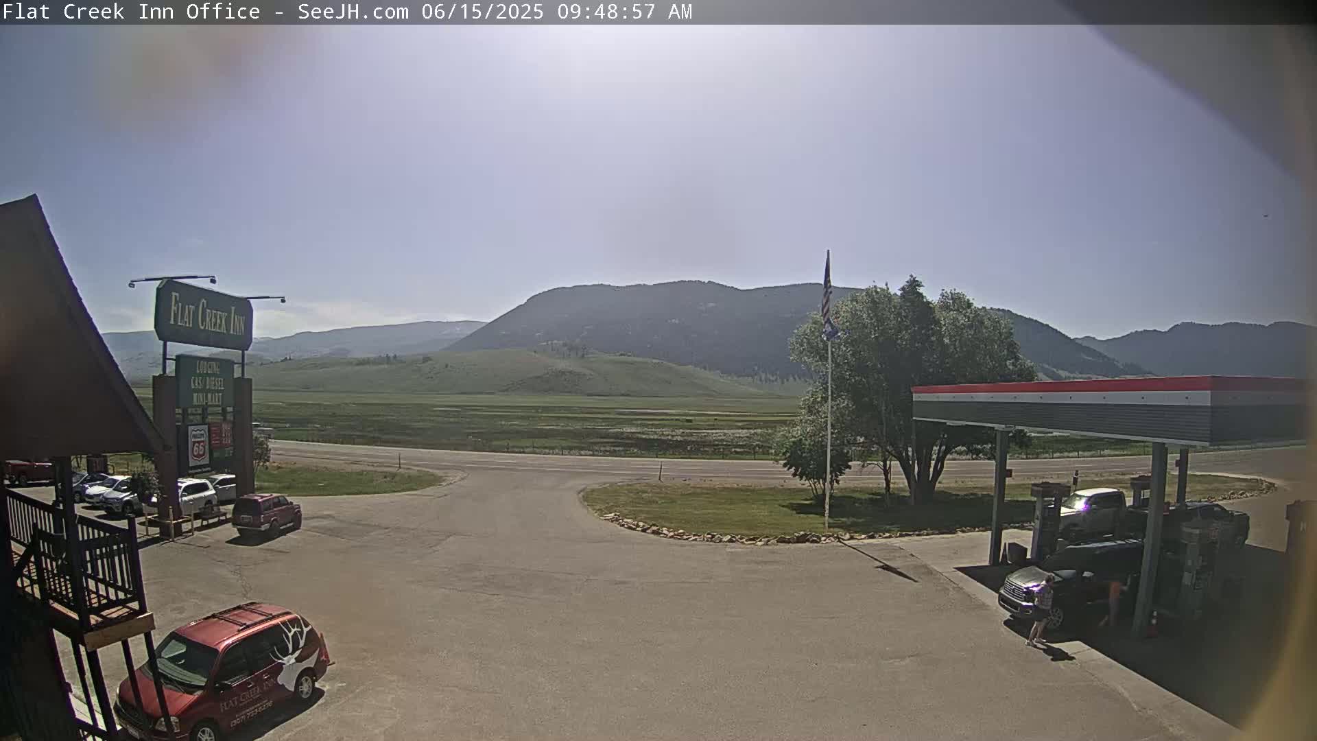 A sunny day reveals a motel parking lot, gas station, and a wide expanse of flat land leading to distant mountains.