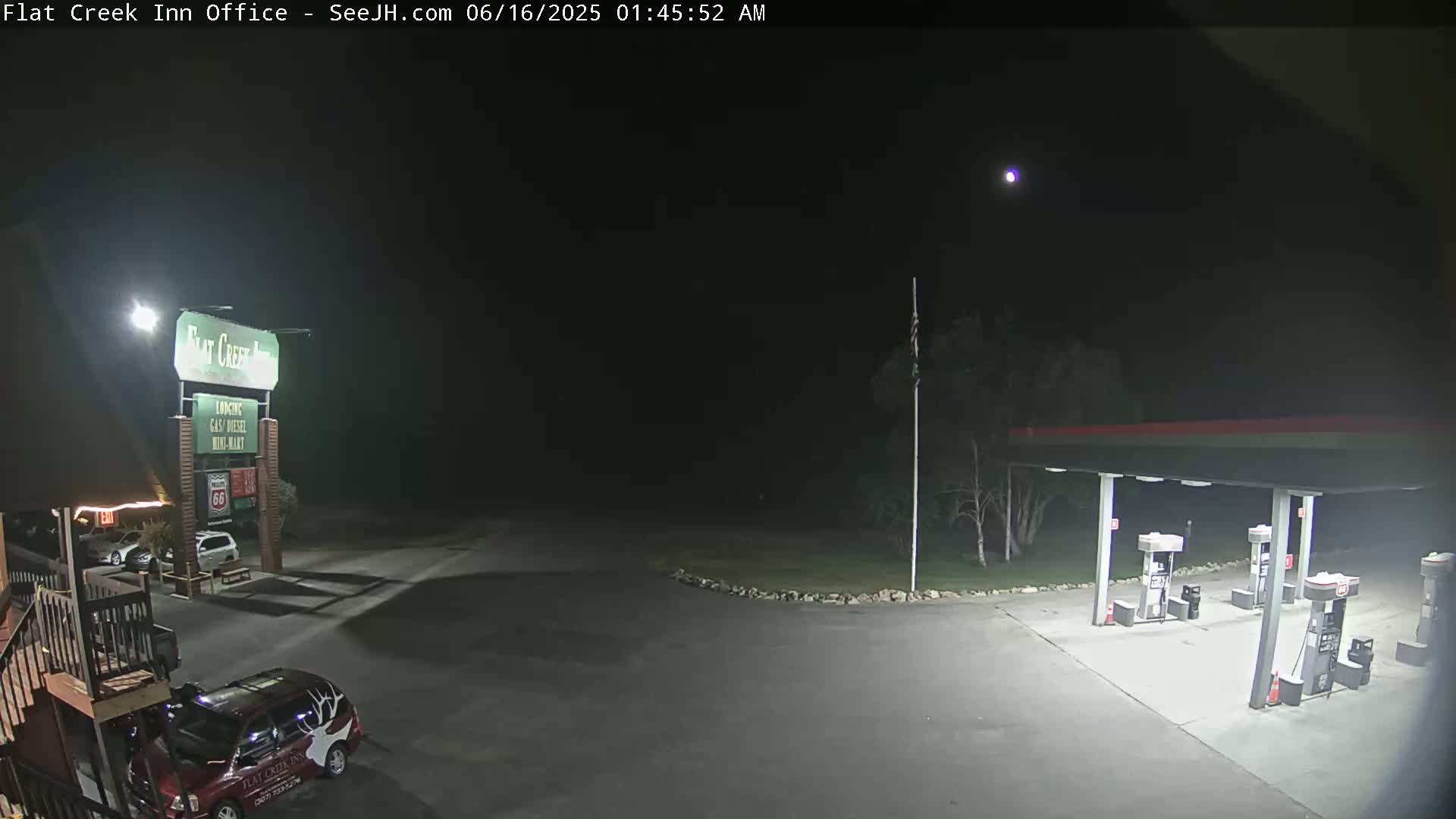 A nighttime view of a gas station and motel parking lot, under a clear, dark sky with a single bright star visible.
