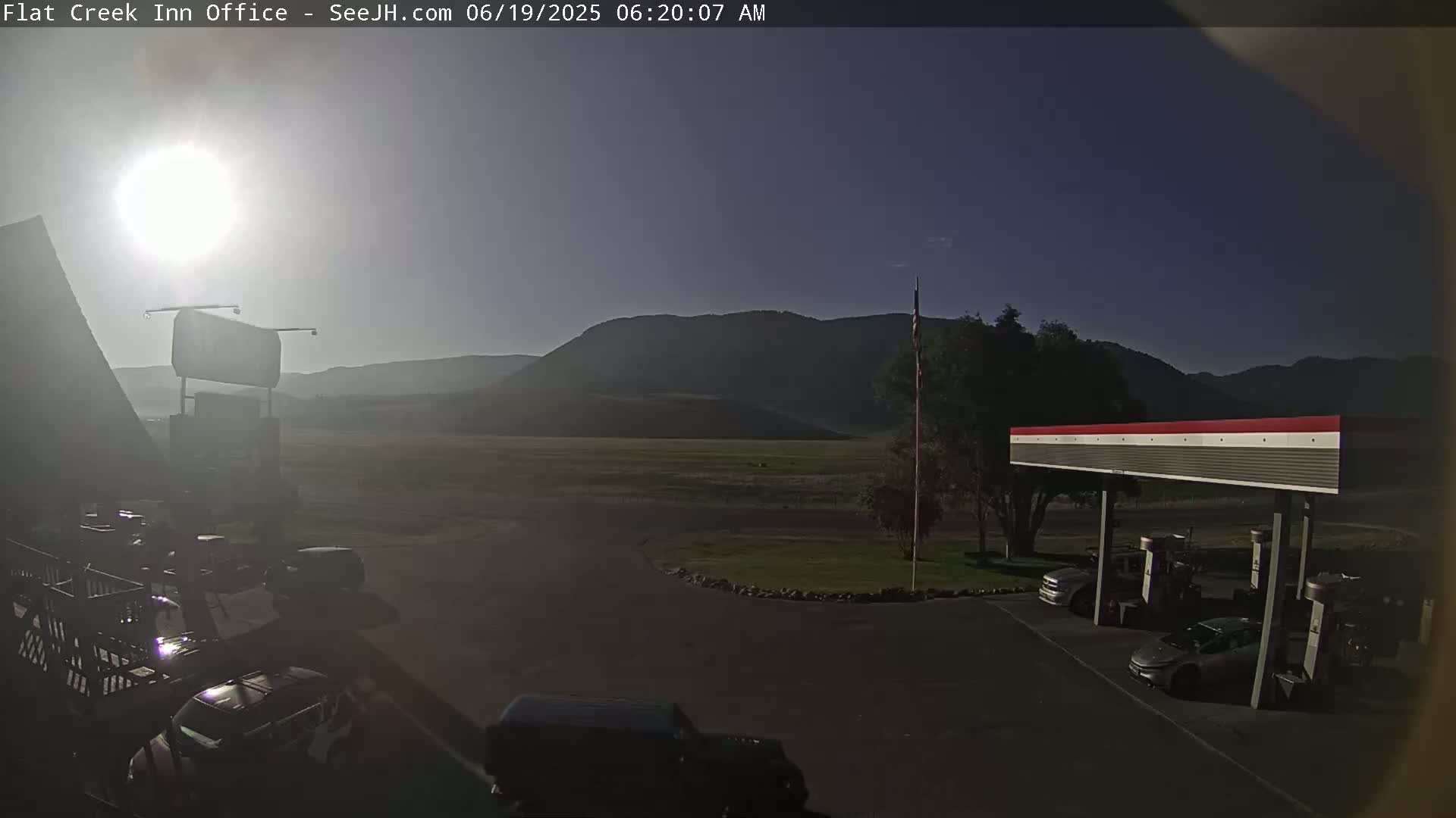 A bright, sunny morning reveals a gas station and several vehicles in a parking lot, with mountains in the background.