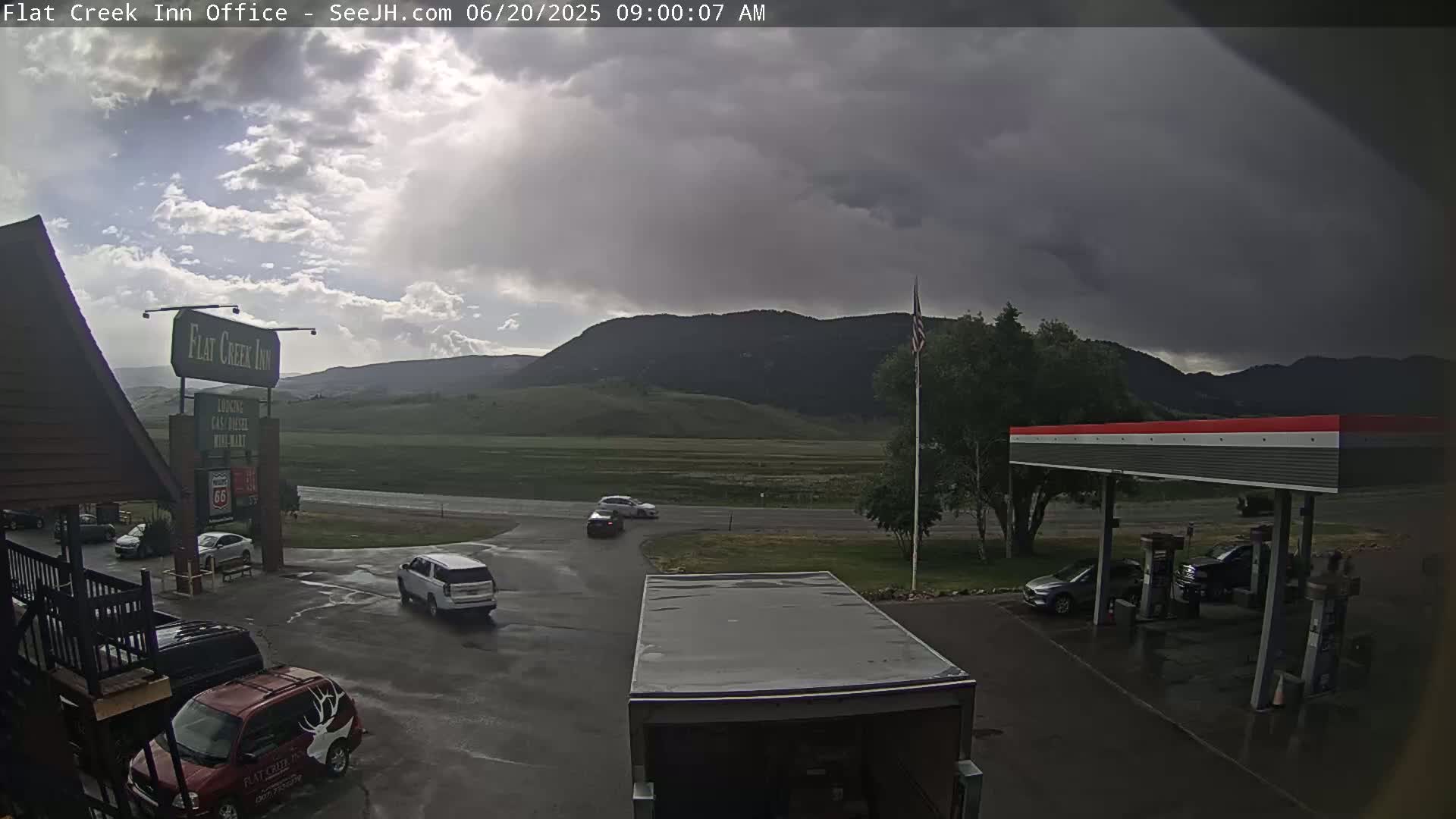 A parking lot with several vehicles, a gas station, and a motel under a dark, cloudy sky.