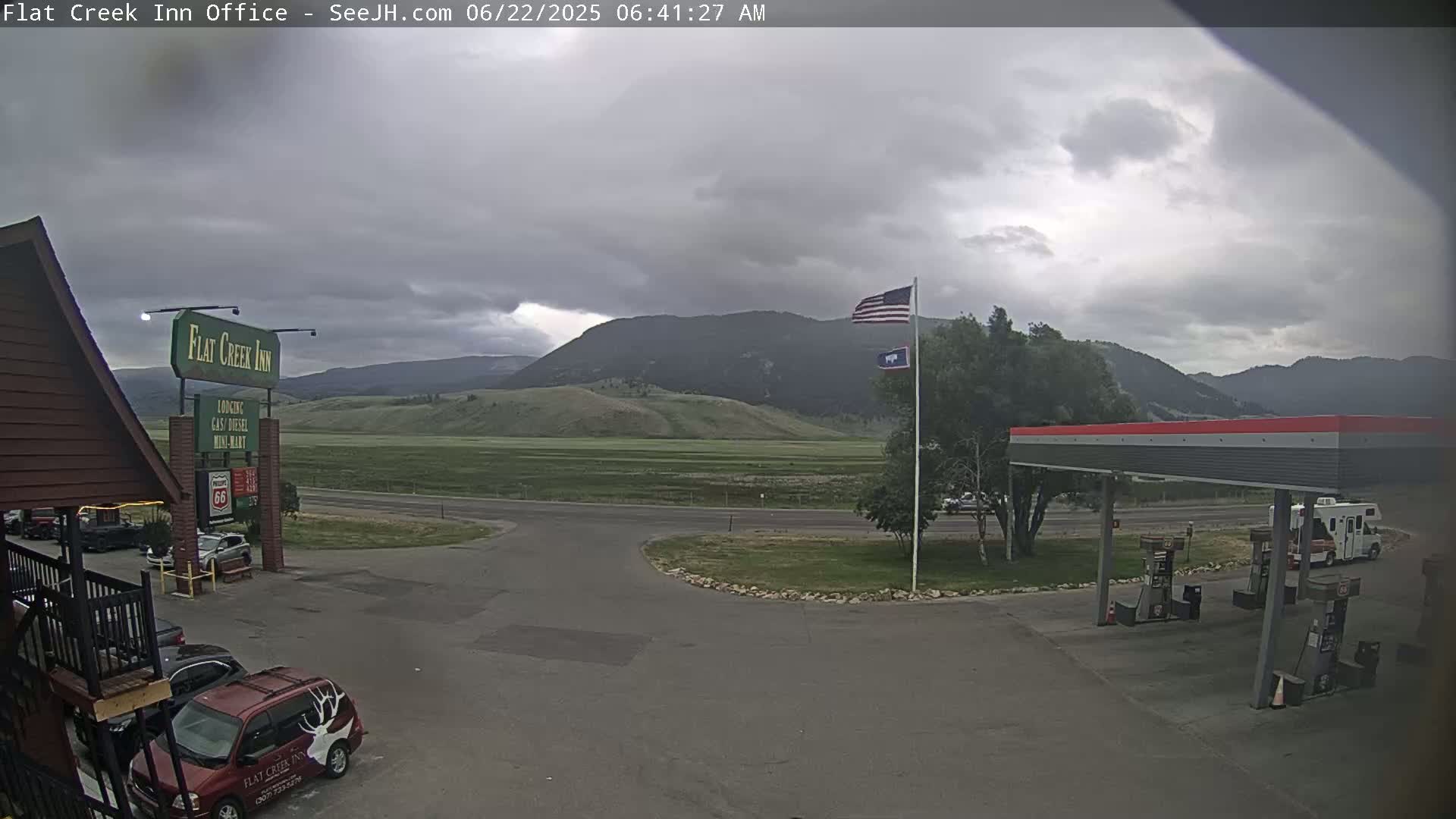 A gas station and motel are situated in a parking lot with a mountainous backdrop under an overcast sky.
