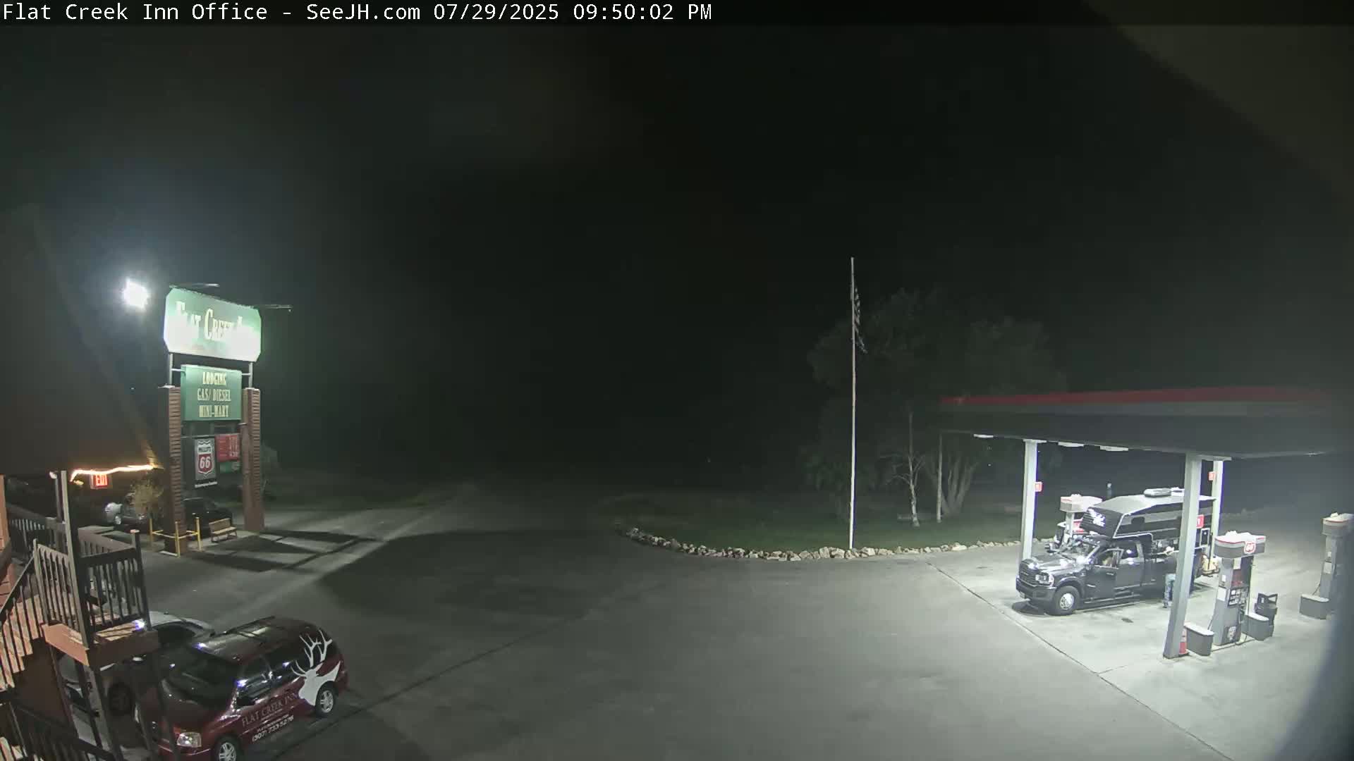 A nighttime view of a gas station and motel parking lot, with a vehicle parked near the motel sign.