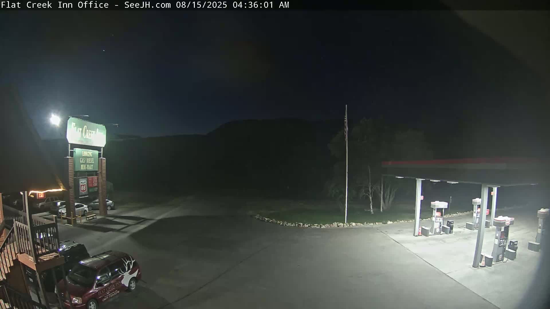 A nighttime view of a gas station and motel parking lot, illuminated by artificial lights.