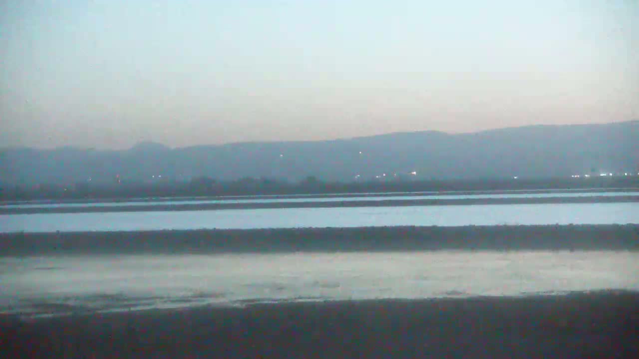 A hazy, twilight view shows flat land with calm water, separated into sections by low dividers, with distant, low-lying hills in the background.