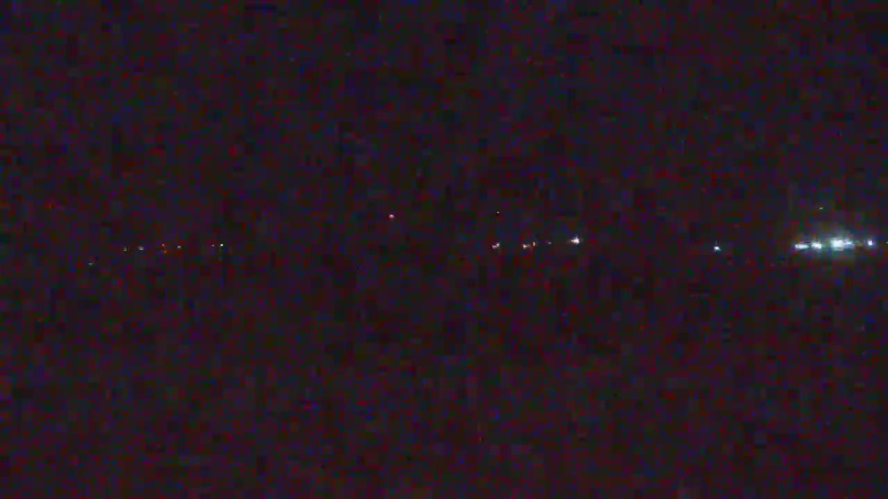 A dark, nighttime scene shows a distant line of faint lights in the darkness.