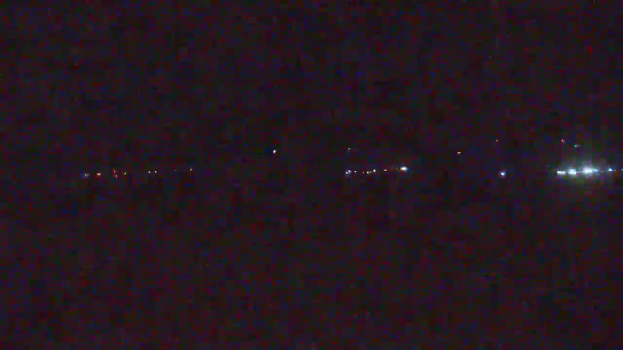 A dark, nighttime scene shows a distant line of faint lights, possibly from vehicles on a road or buildings.
