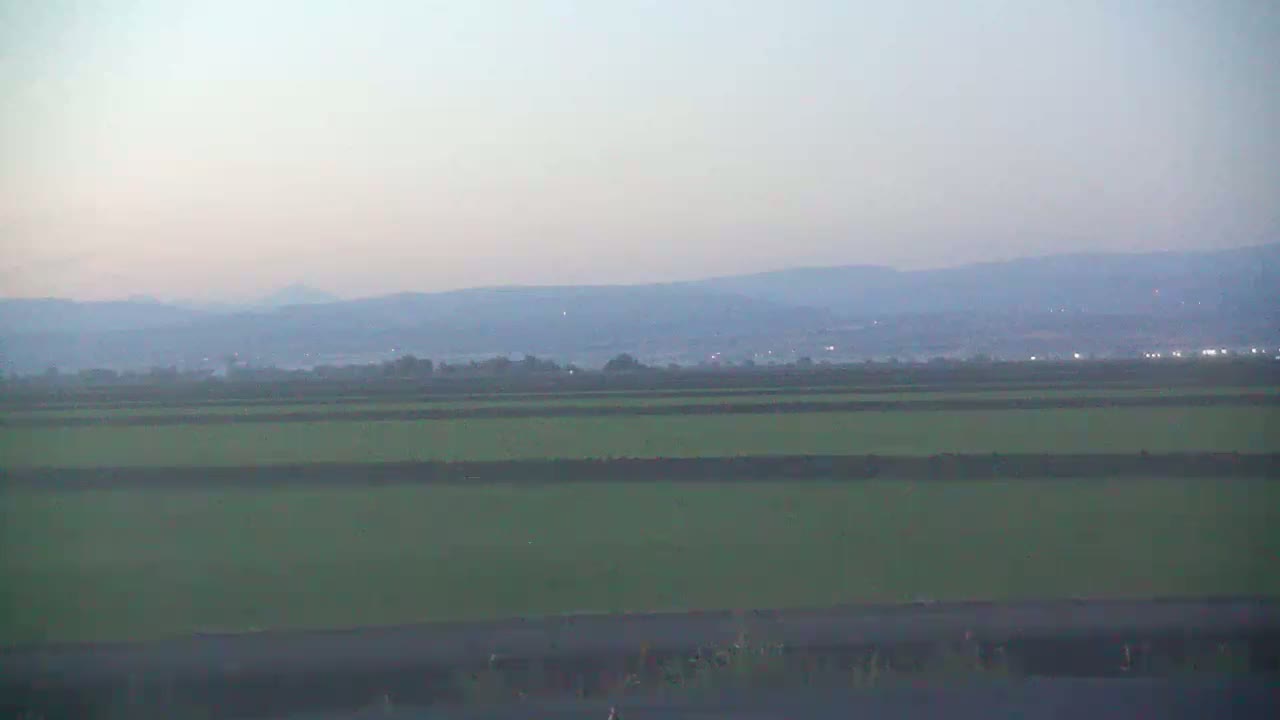 A hazy, flat expanse of green fields stretches to a distant range of low mountains under a pale sky.