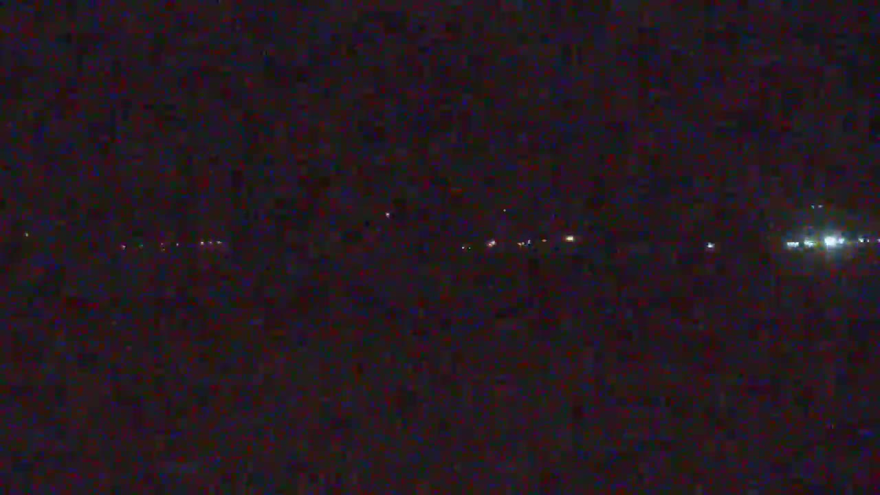 A dark, nighttime scene shows a distant line of faint lights across a mostly black landscape.