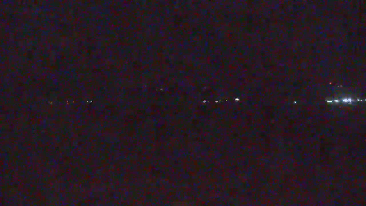 A dark, nighttime landscape shows a distant line of faint lights under a seemingly clear sky.