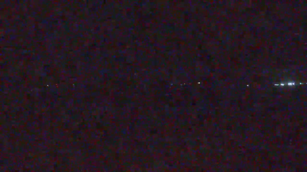 A nighttime long shot shows a distant line of faint lights across a dark, possibly obscured, landscape.