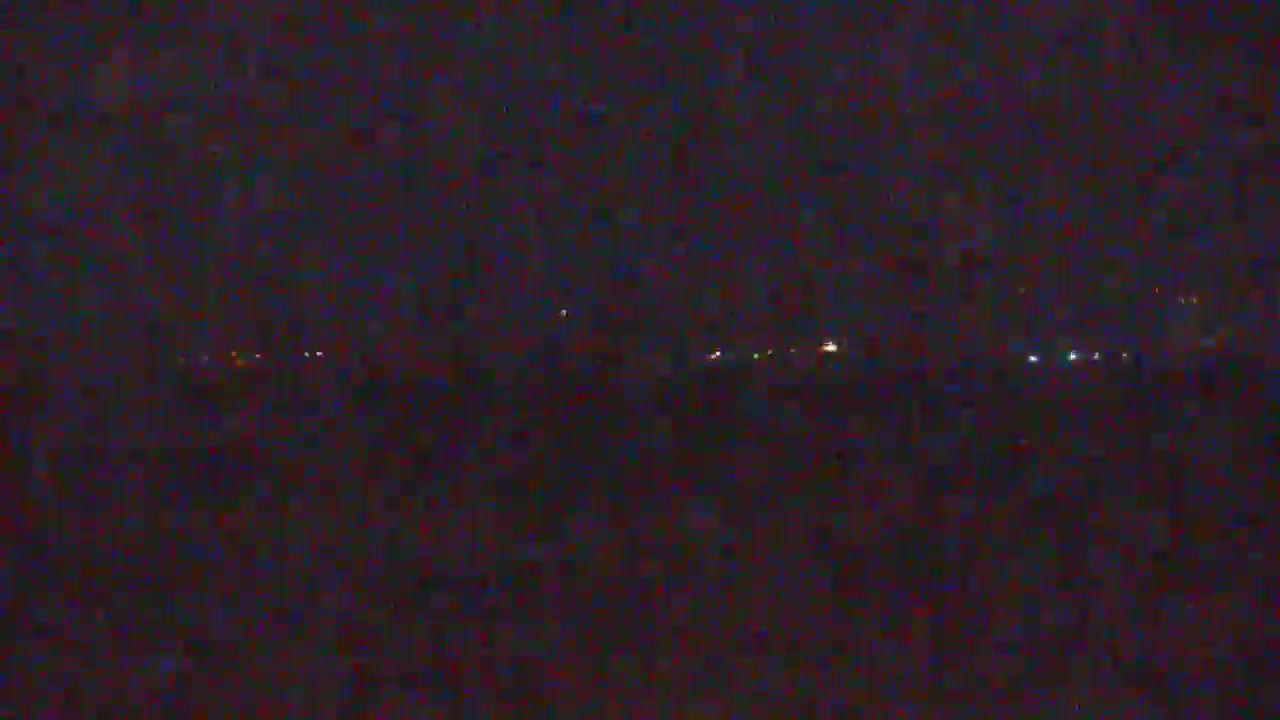 A dark, nighttime landscape shows a faint line of distant lights on the horizon.