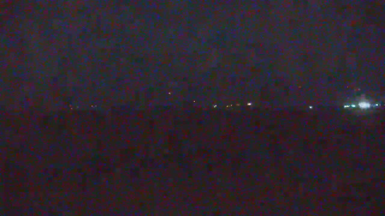 A dark, nighttime scene shows a distant line of faint lights against a mostly obscured horizon.