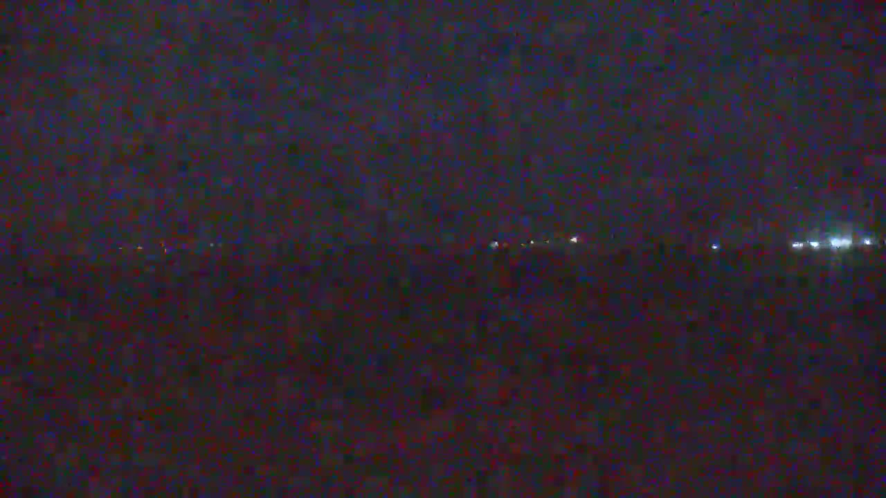A dark, nighttime landscape shows a faint horizon line with a few distant lights.