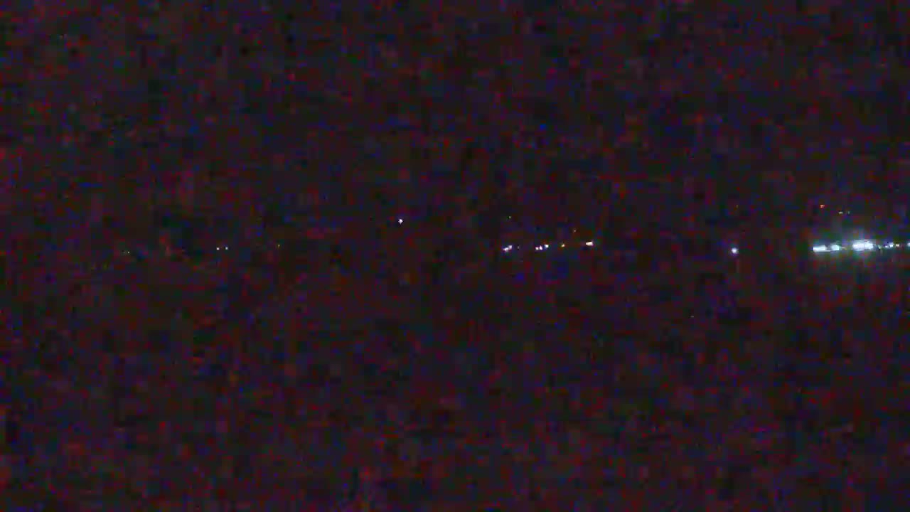 A dark, nighttime scene shows a distant line of lights, possibly from vehicles or buildings, on a seemingly flat landscape.