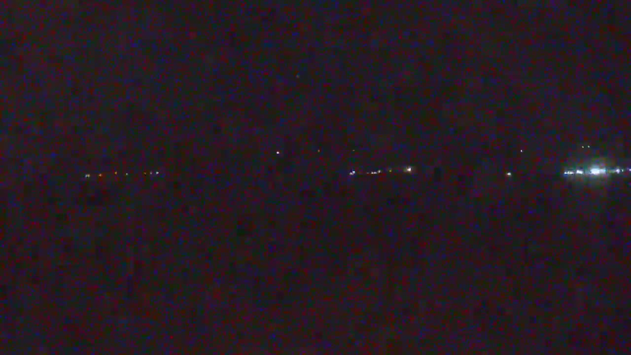A dark, nighttime scene shows a distant line of faint lights, possibly from vehicles or buildings.