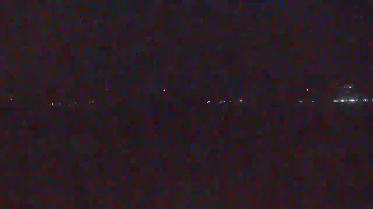 A dark, nighttime scene shows a distant line of faint lights on the horizon.