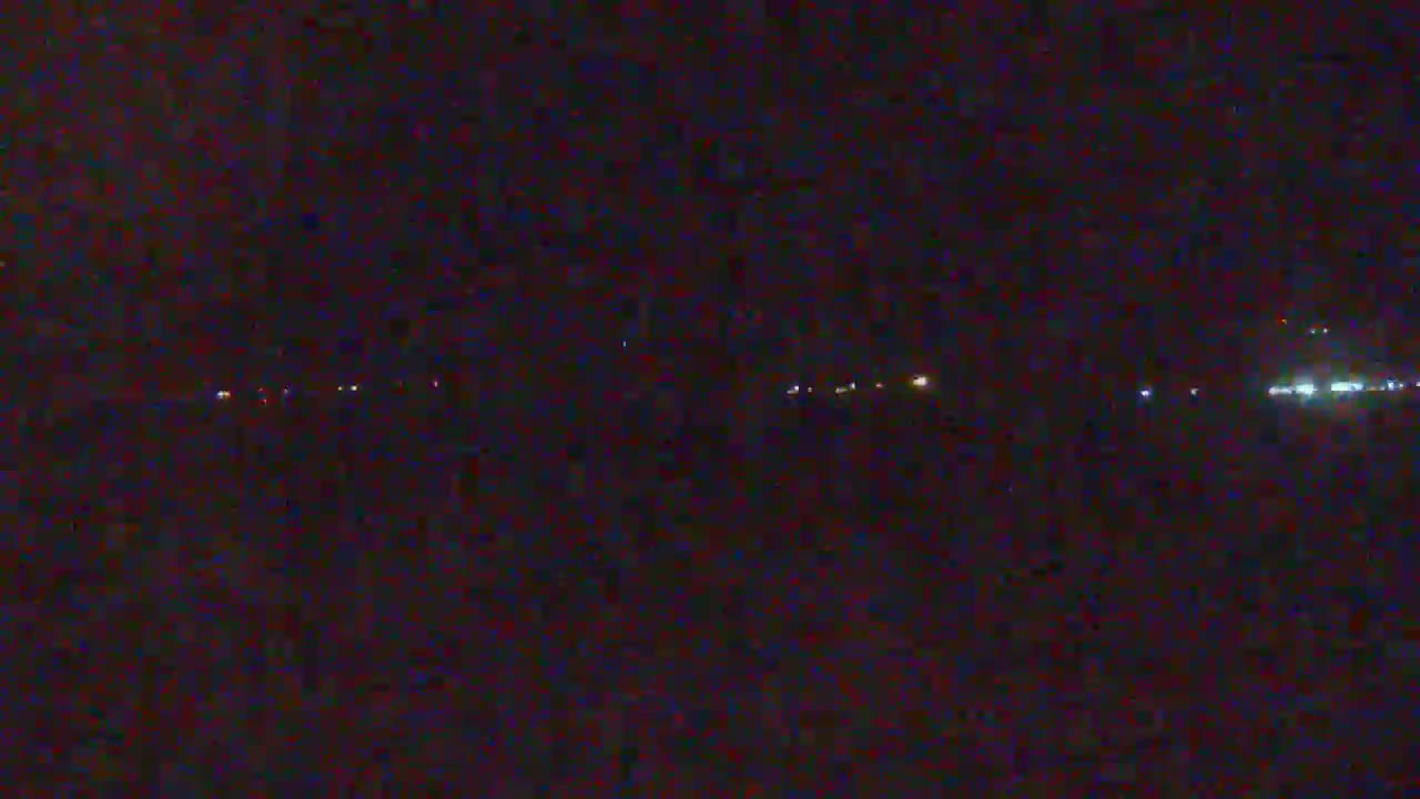 A dark, nighttime scene shows a line of distant lights possibly from vehicles or buildings.