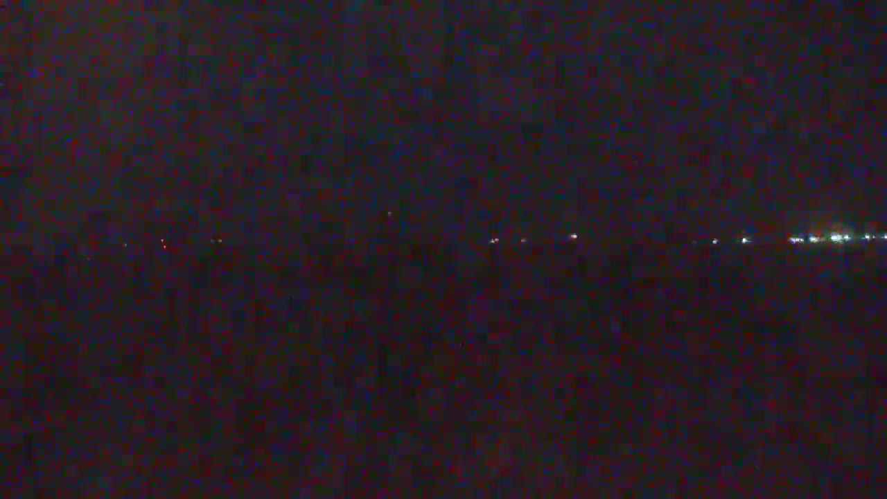 A dark, nighttime scene shows a distant line of lights on the horizon.